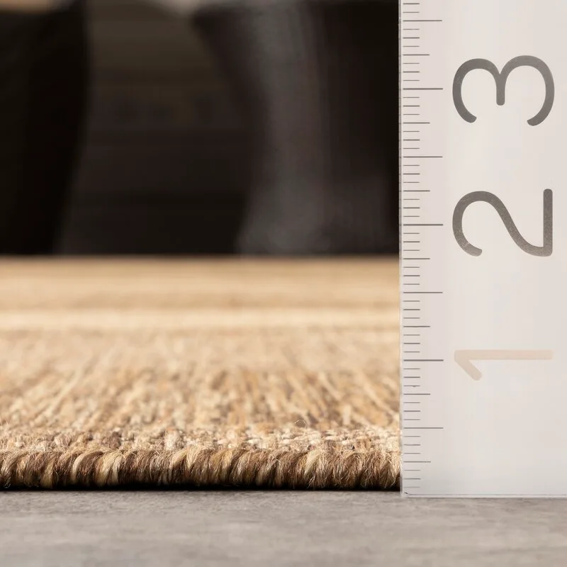 A close-up of a brown woven rug sample on a gray floor next to a vertical measuring ruler.