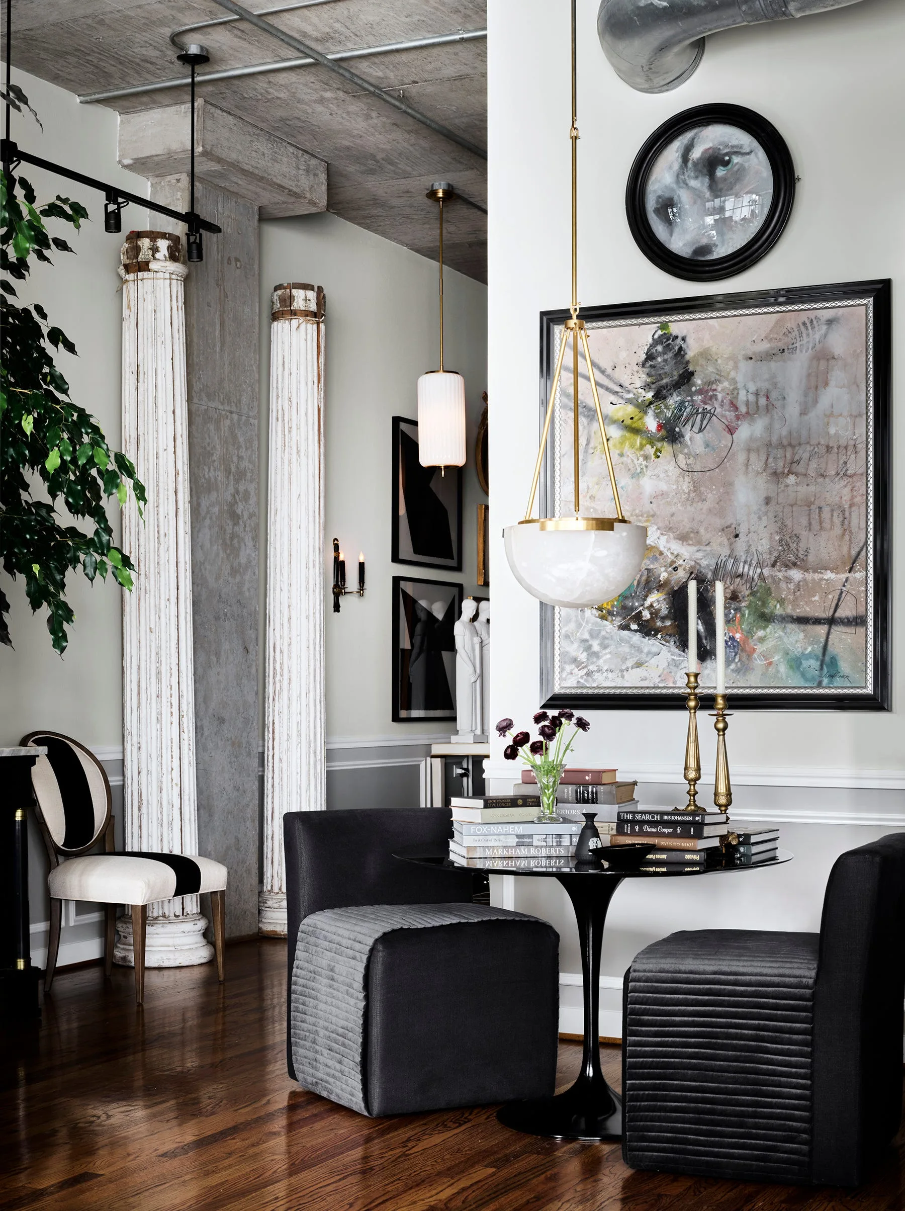 A dining nook features a black pedestal table and matching upholstered chairs set against a wall with a large abstract painting.