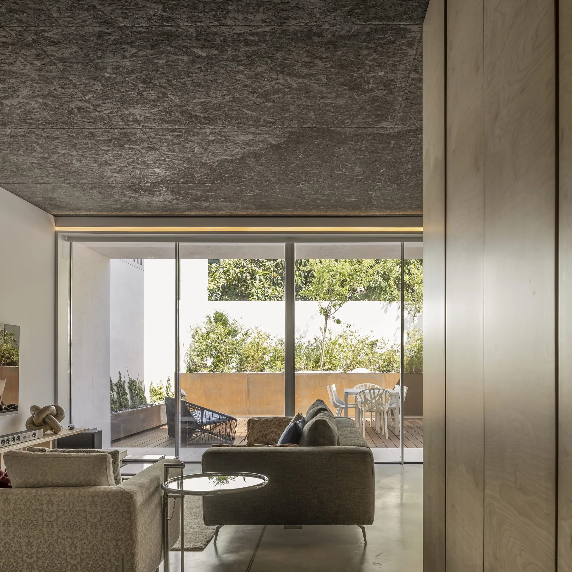 A modern living room features a textured gray ceiling, a fabric sofa, and large sliding glass doors leading to an outdoor patio with dining furniture.