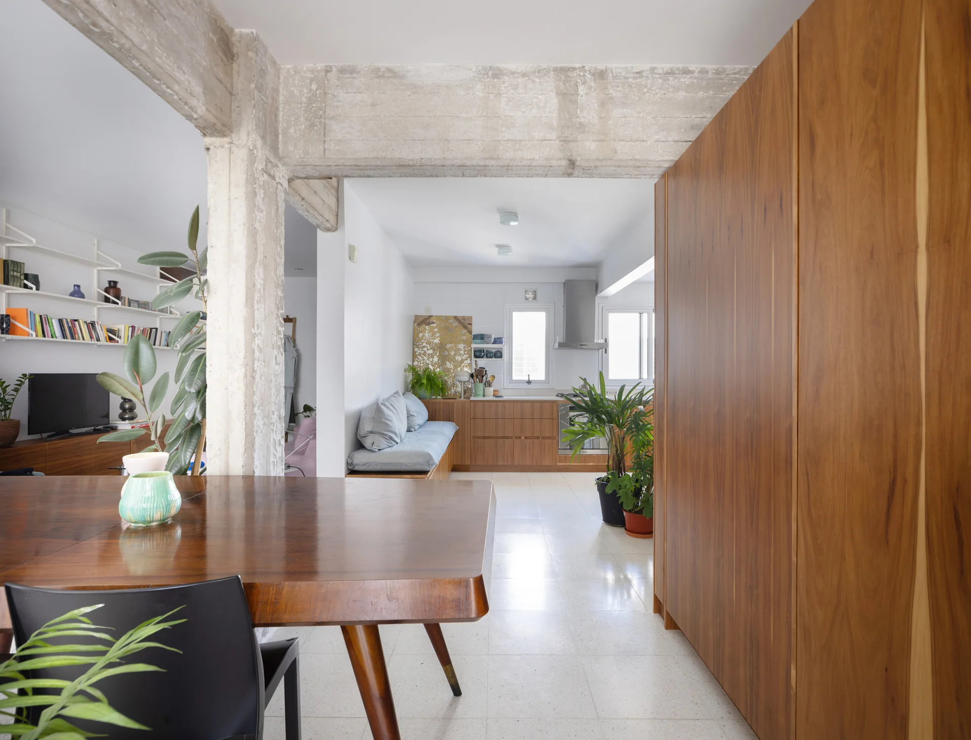 An open floor plan room features a large wood dining table, an exposed concrete beam, and warm wood kitchen cabinetry.