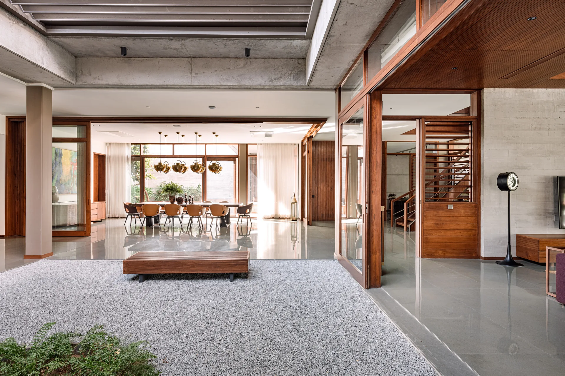 A modern home interior with a grey gravel courtyard and wood bench, bordered by polished floors and large wood-framed glass sliding doors.