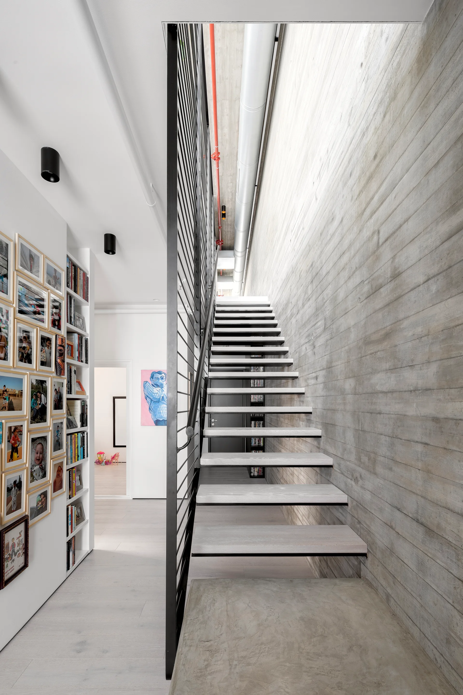 An industrial floating staircase with light wood treads and a black metal railing built against a textured board-formed concrete wall.