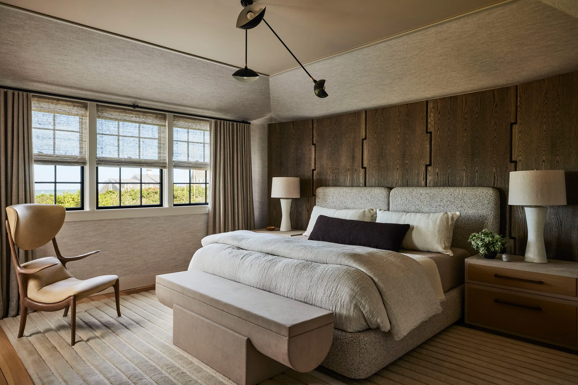 An organic modern bedroom featuring an upholstered bed against notched wood wall paneling, a matching bench, and a sculptural wood and leather chair.