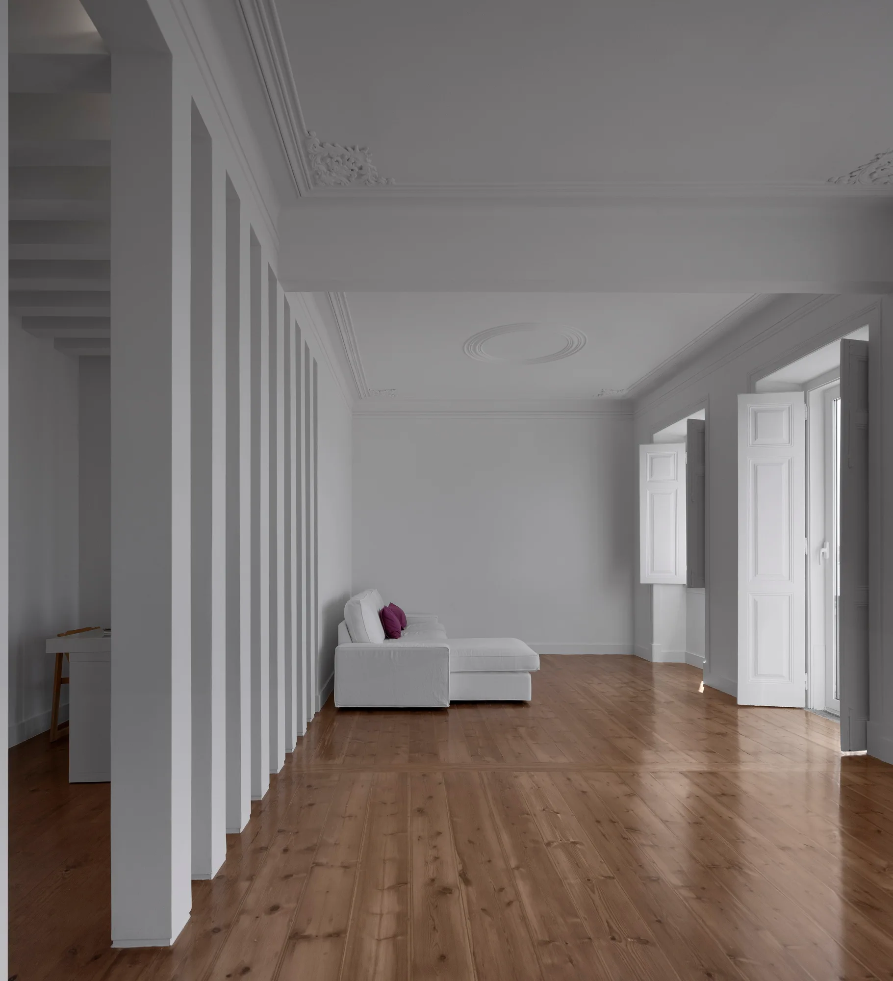 A bright white minimalist living room features a vertical pillar partition wall, hardwood floors, and a white sofa with purple accent pillows.
