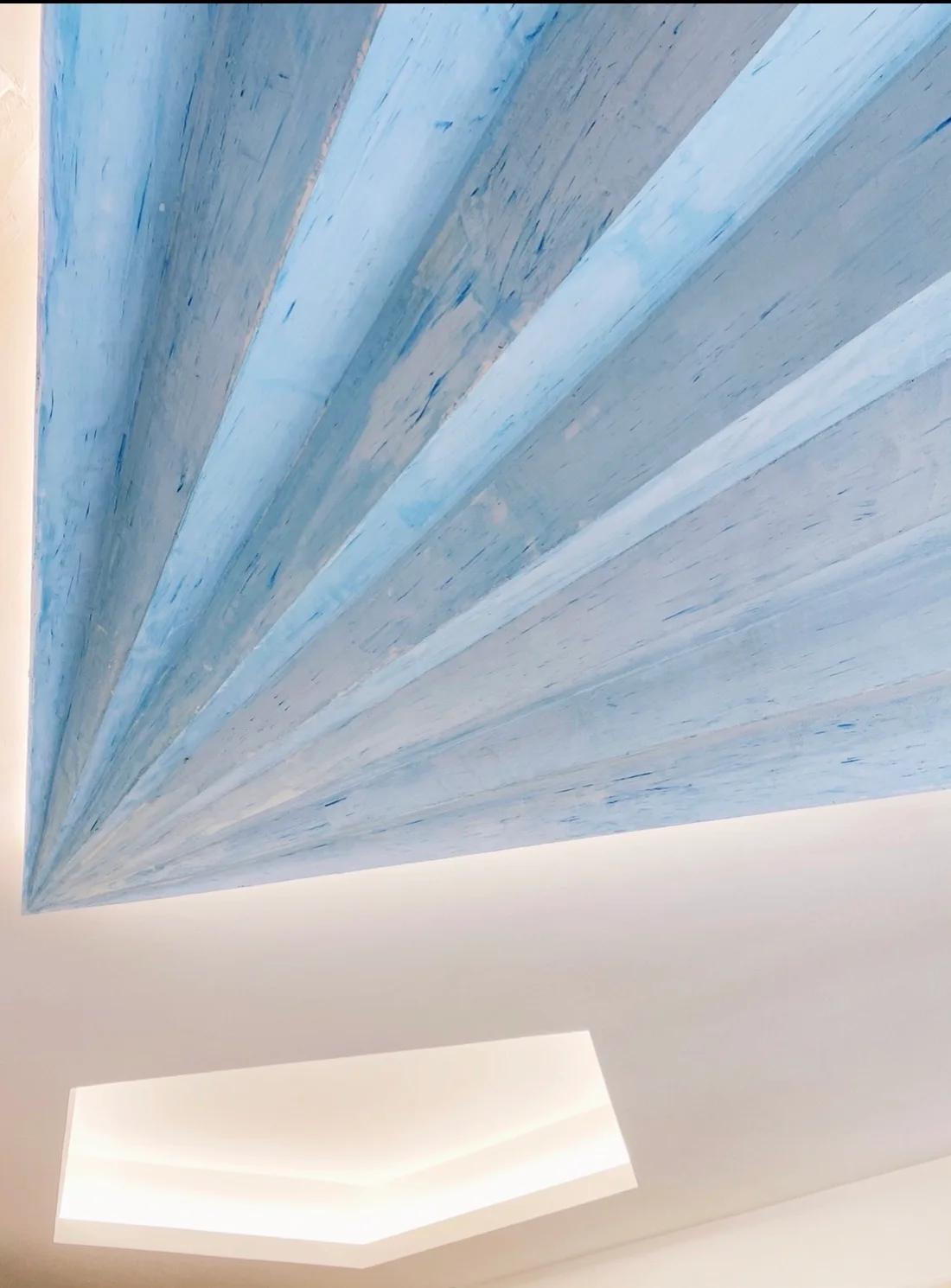Angled ceiling panels painted with a textured blue finish converge above a white recessed light alcove.
