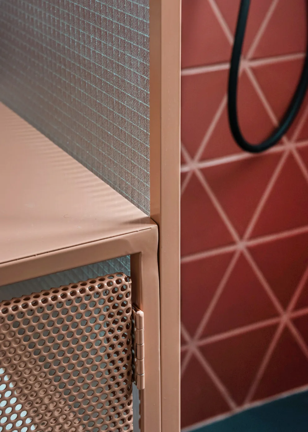 A close-up shows a peach-colored perforated metal cabinet unit paired with a background wall of red triangular geometric tiles.