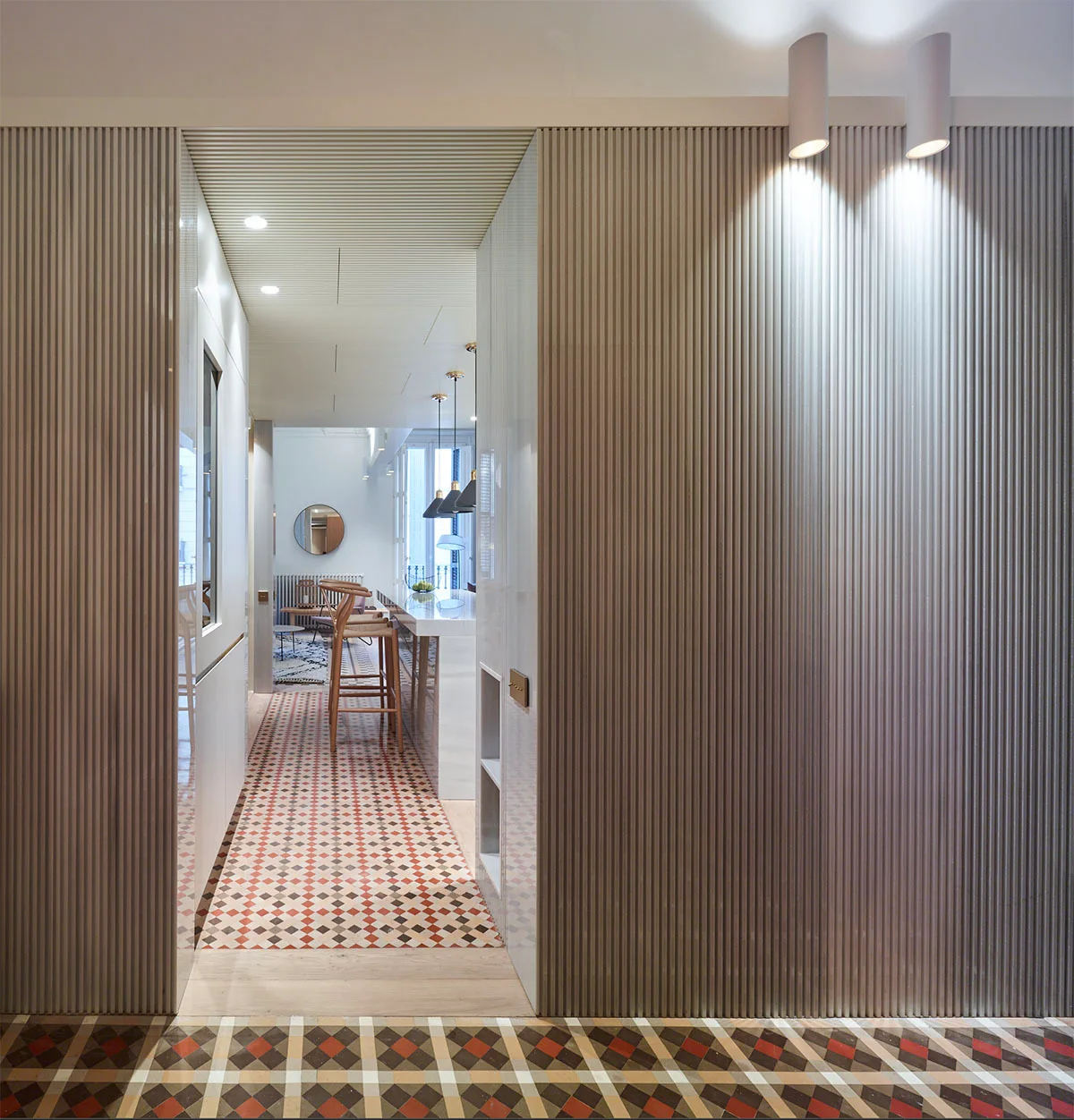 A narrow hallway with beige fluted wall paneling and a geometric diamond-patterned tile floor leads into a kitchen.