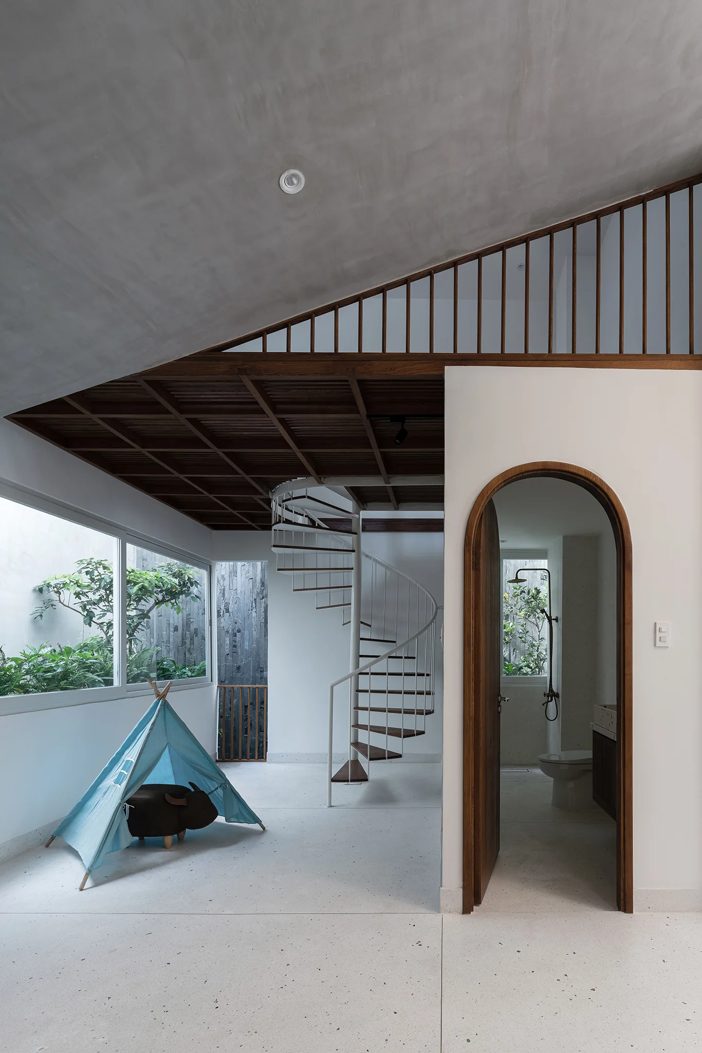 A modern playroom featuring a white spiral staircase, a blue teepee play tent, and a wooden arched doorway leading to a bathroom.