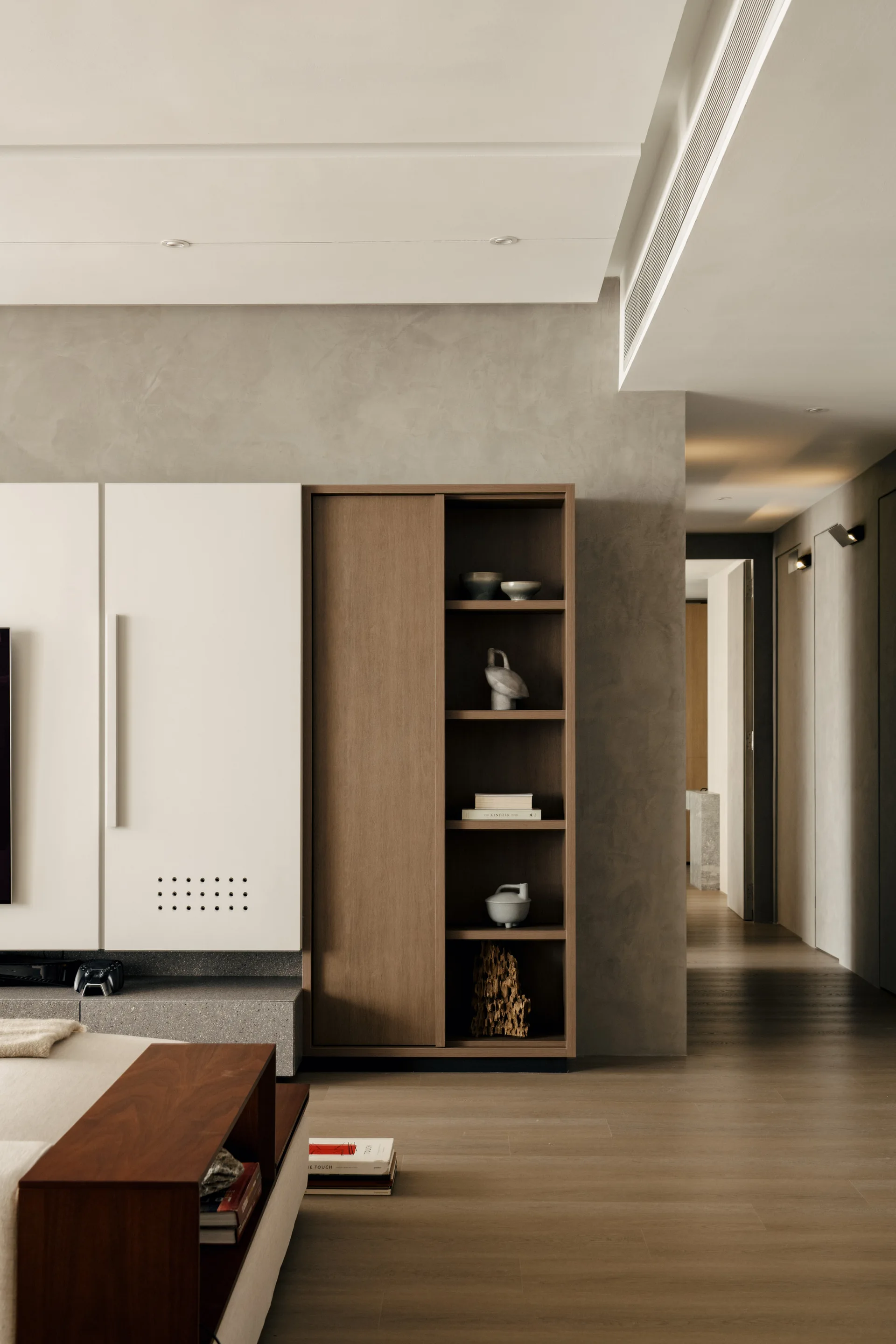A minimalist living room with custom white and wood built-in cabinetry set against a textured grey plaster wall near a hallway entrance.