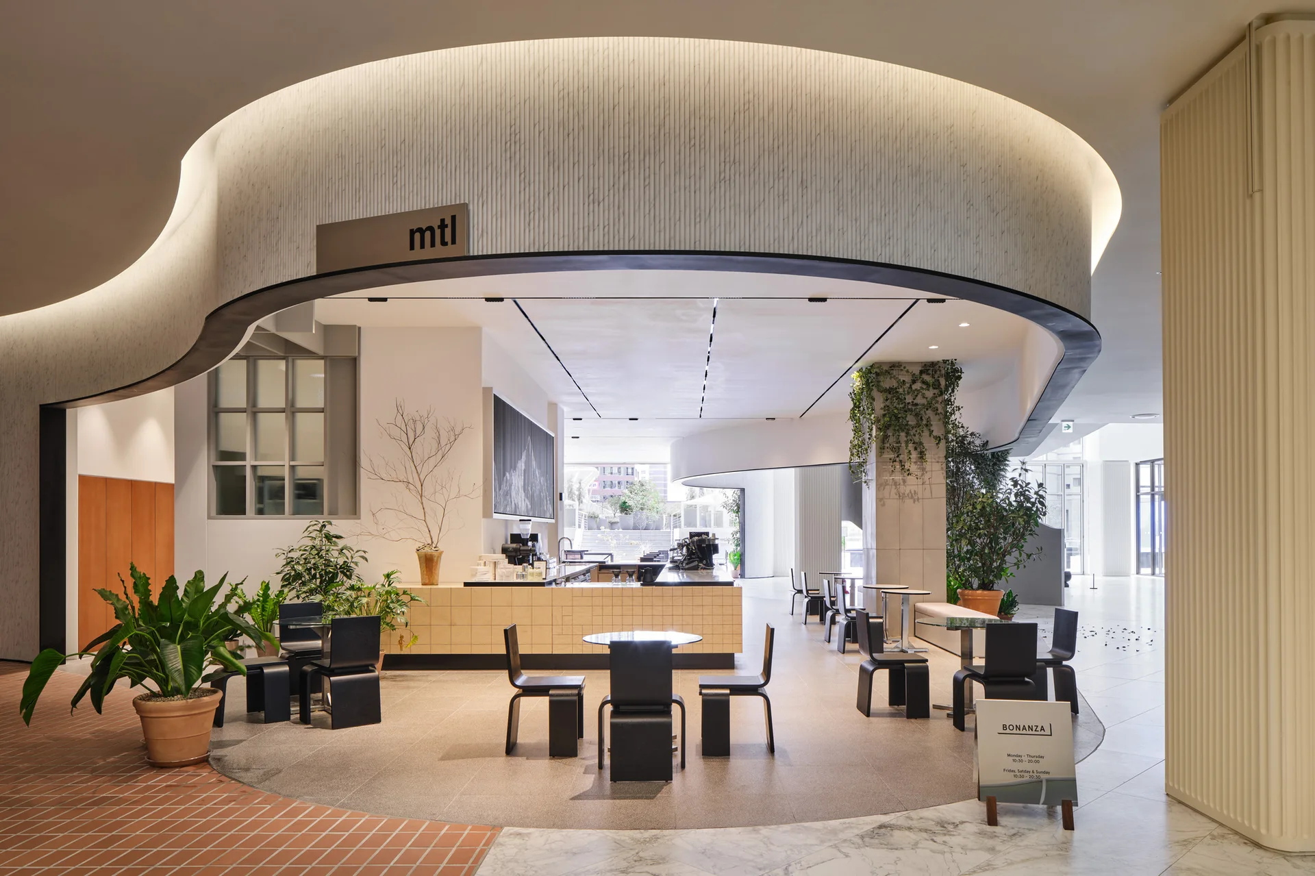 A modern cafe interior features a large curved ceiling canopy with cove lighting over black minimalist tables and chairs.