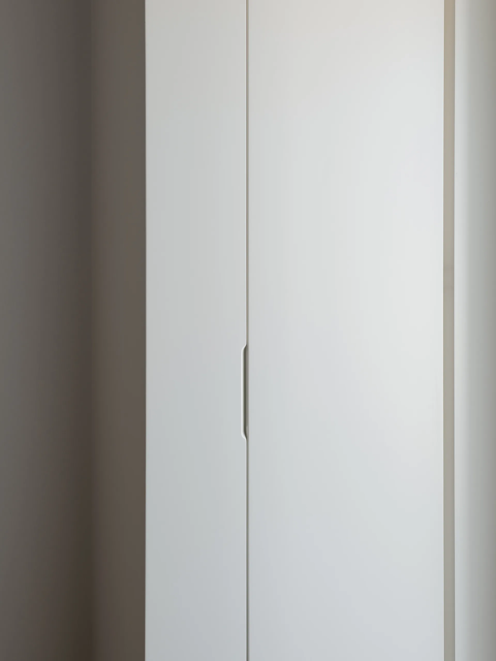 A close-up view of a minimalist white flat-panel cabinet door featuring a vertical recessed pull handle cutout.
