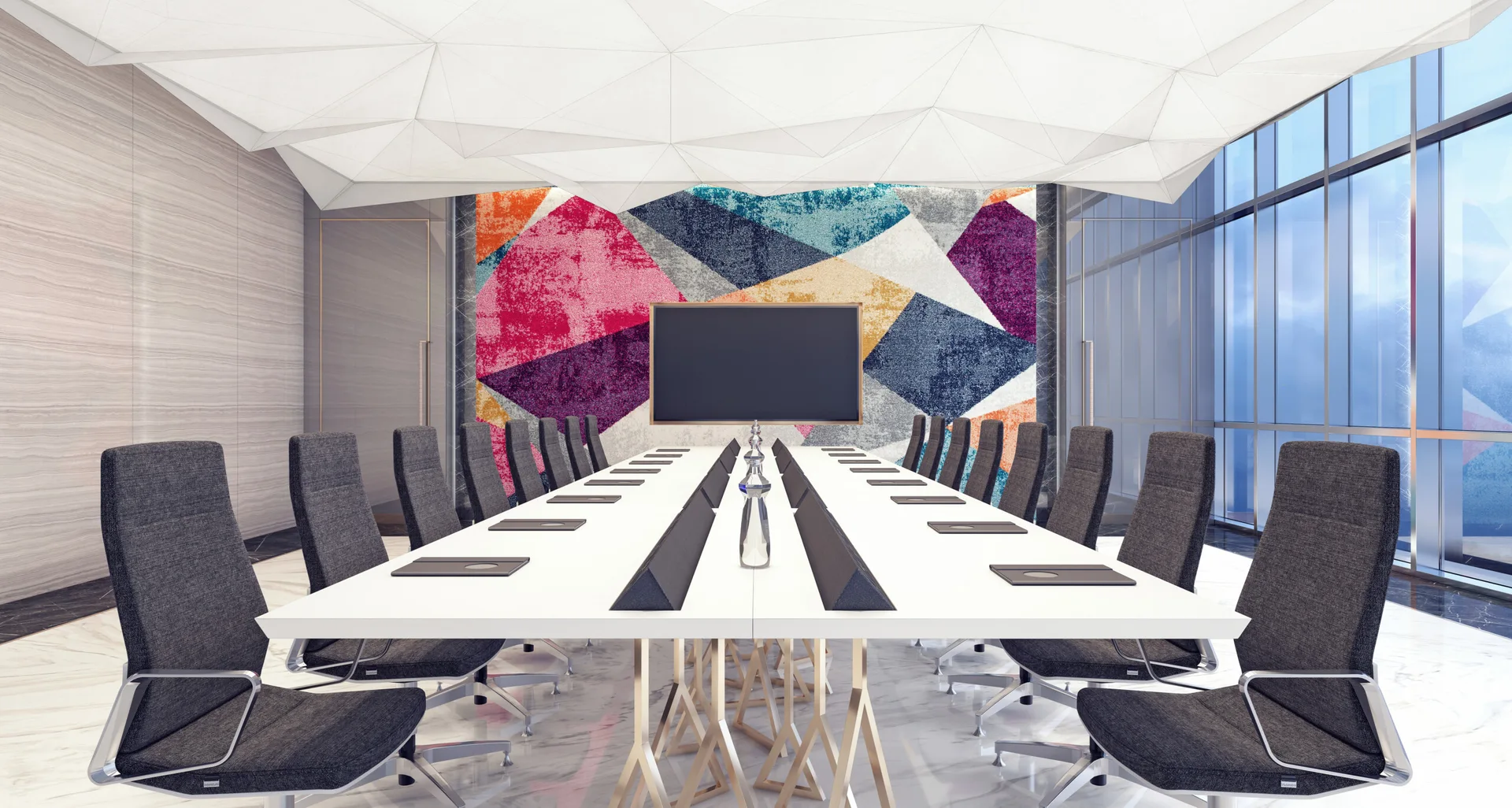 A long white conference table and gray chairs sit beneath a faceted white ceiling in a room featuring a colorful geometric mural wall.