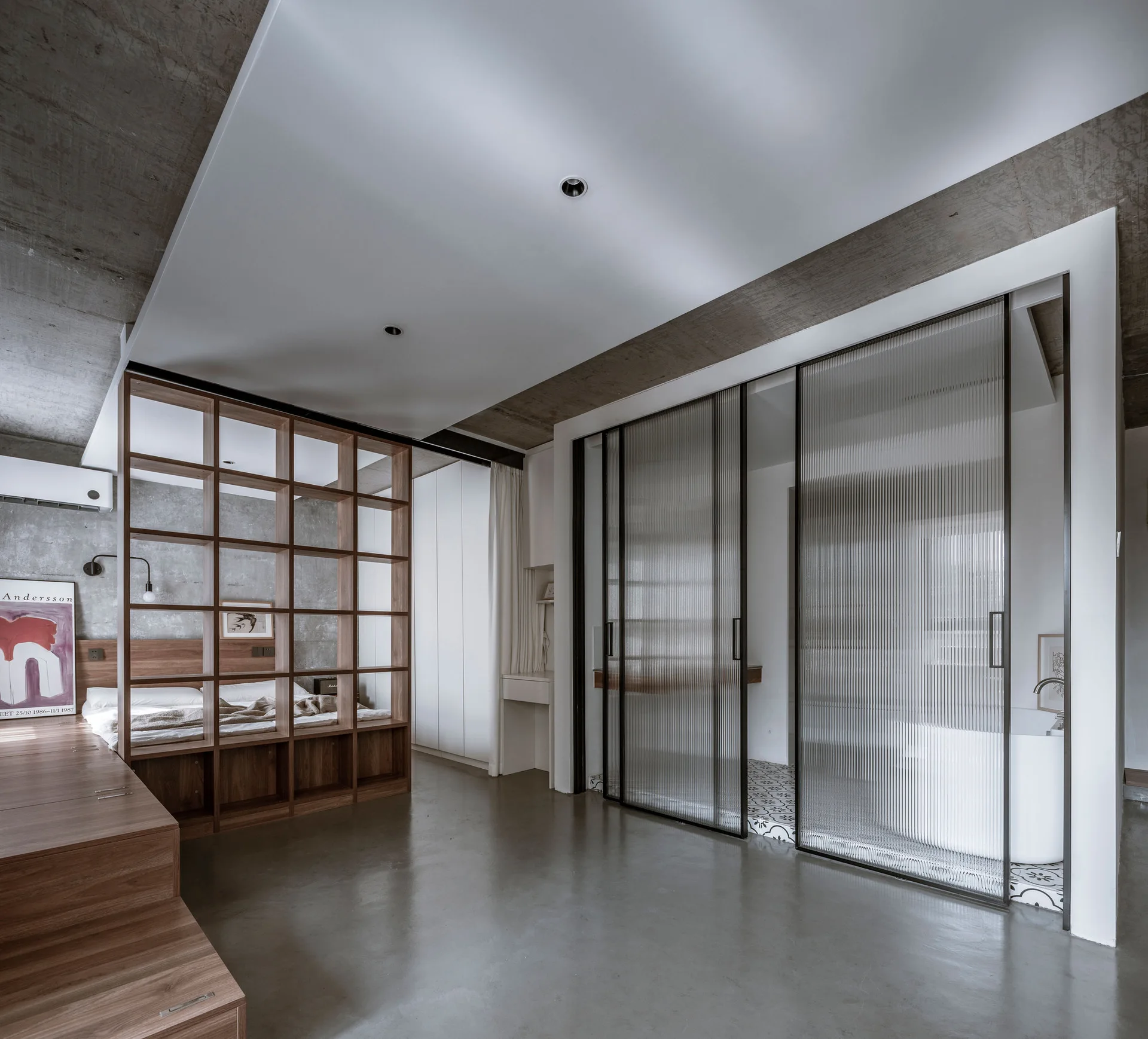 A modern bedroom features a wooden grid room divider, a platform bed, and black-framed fluted glass sliding doors opening to a bathroom.