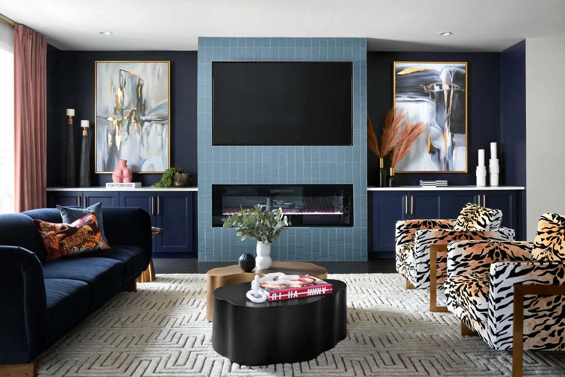 A living room features a blue vertical tile fireplace, navy blue built-in cabinets, abstract art, a navy velvet sofa, and tiger-print armchairs.
