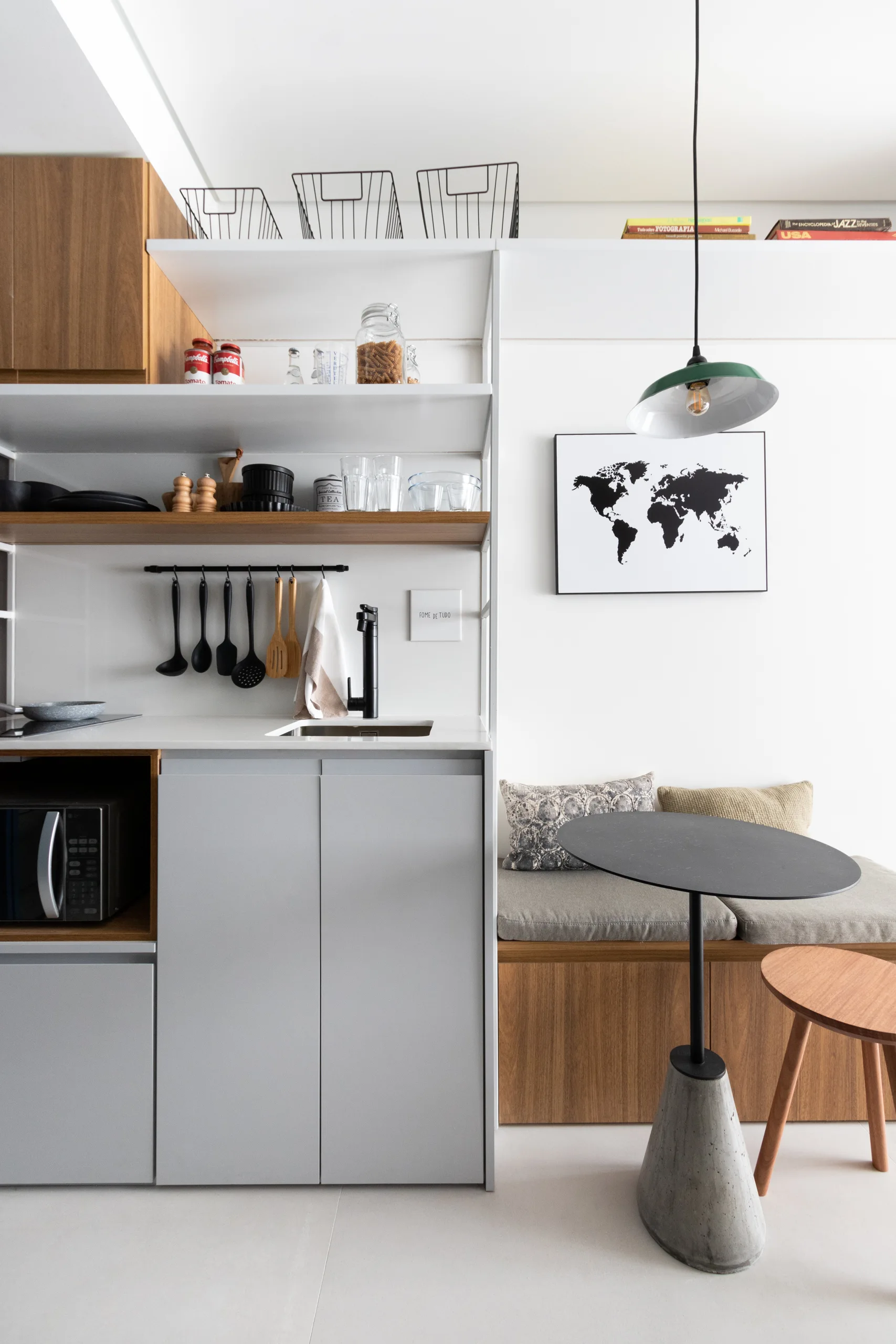 A modern kitchenette with matte grey cabinets, a built-in wooden banquette bench, open shelving, and a small black bistro table with a concrete base.