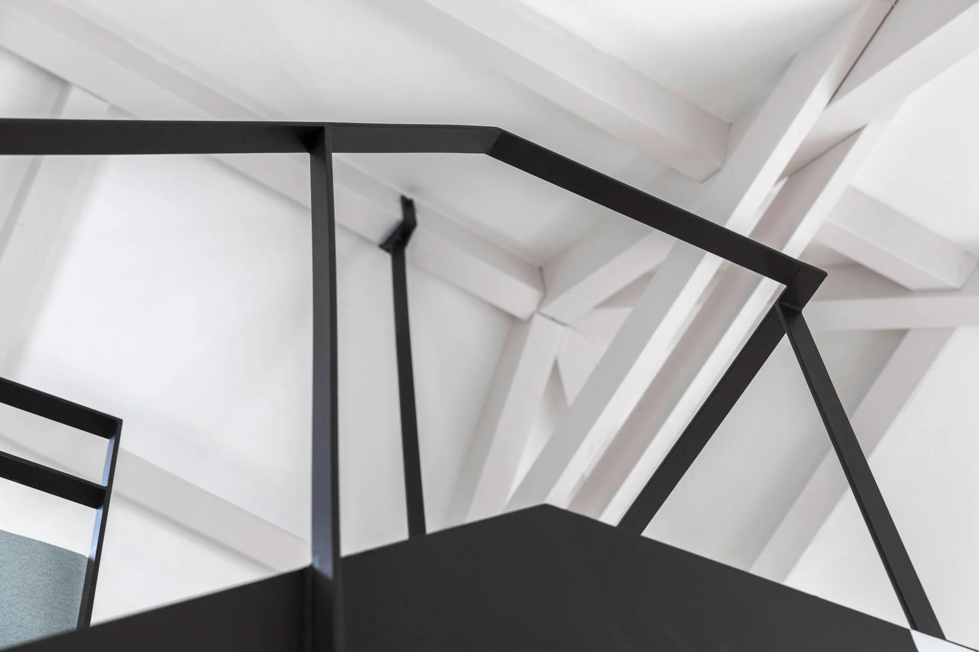 A close-up shot of a minimalist black metal stair railing set against a background of white painted structural ceiling beams.