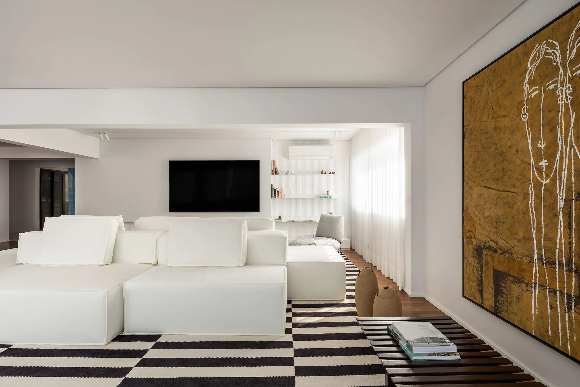 A modern white living room featuring a large modular sectional sofa on a bold black and white striped rug next to a large gold abstract wall painting.