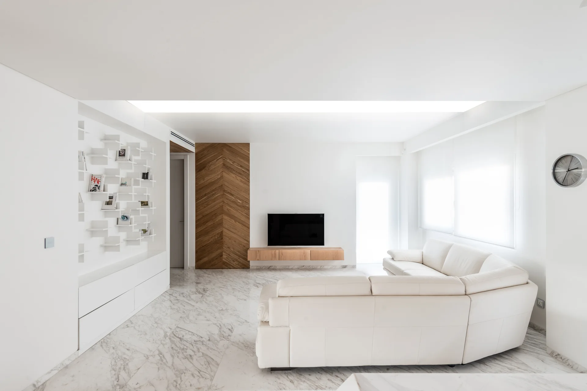 A modern white living room featuring a curved sectional sofa, polished marble flooring, a floating wood console, and a herringbone accent wall.