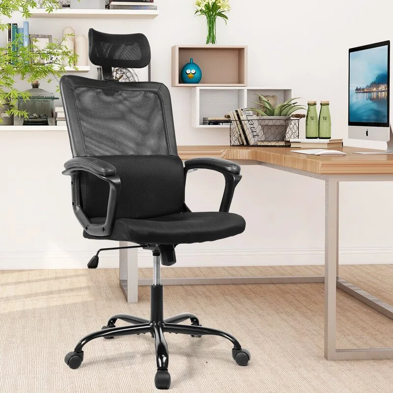 A black mesh ergonomic office chair with a headrest stands in front of a light wood desk in a bright home office.