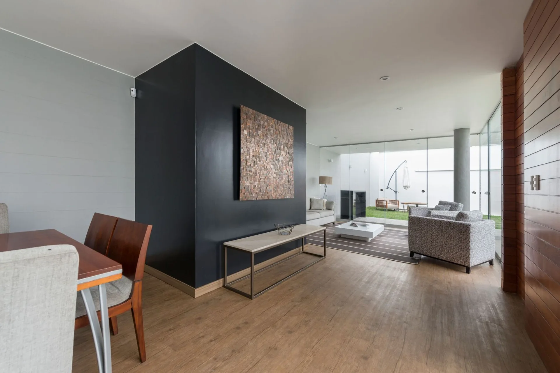 A modern open-concept living space features a bold black room divider with textured wooden art, a stone-topped console table, and glass walls.