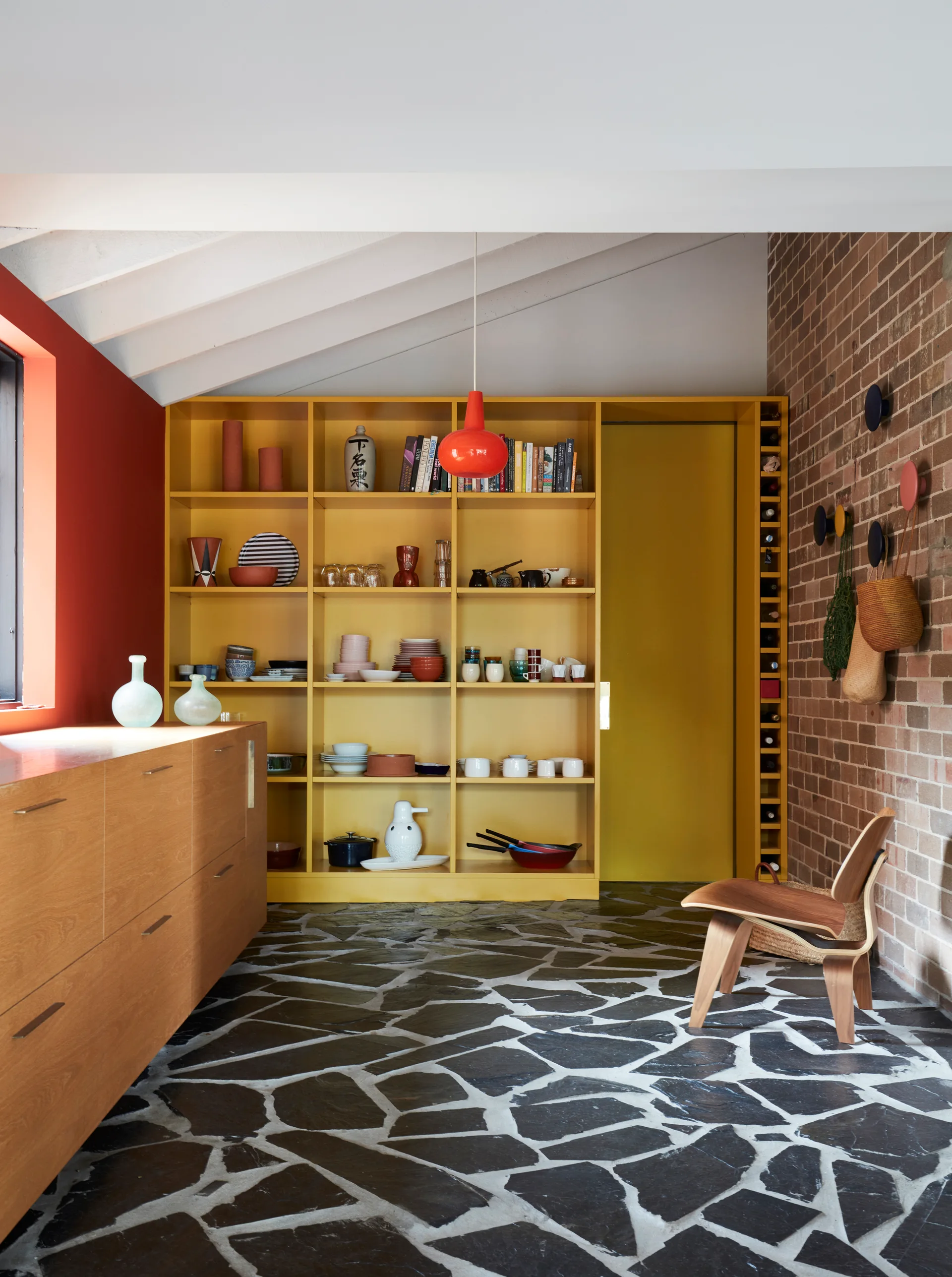 A kitchen featuring a large yellow shelving unit, wood cabinetry, a brick wall, and dark irregular stone flooring.