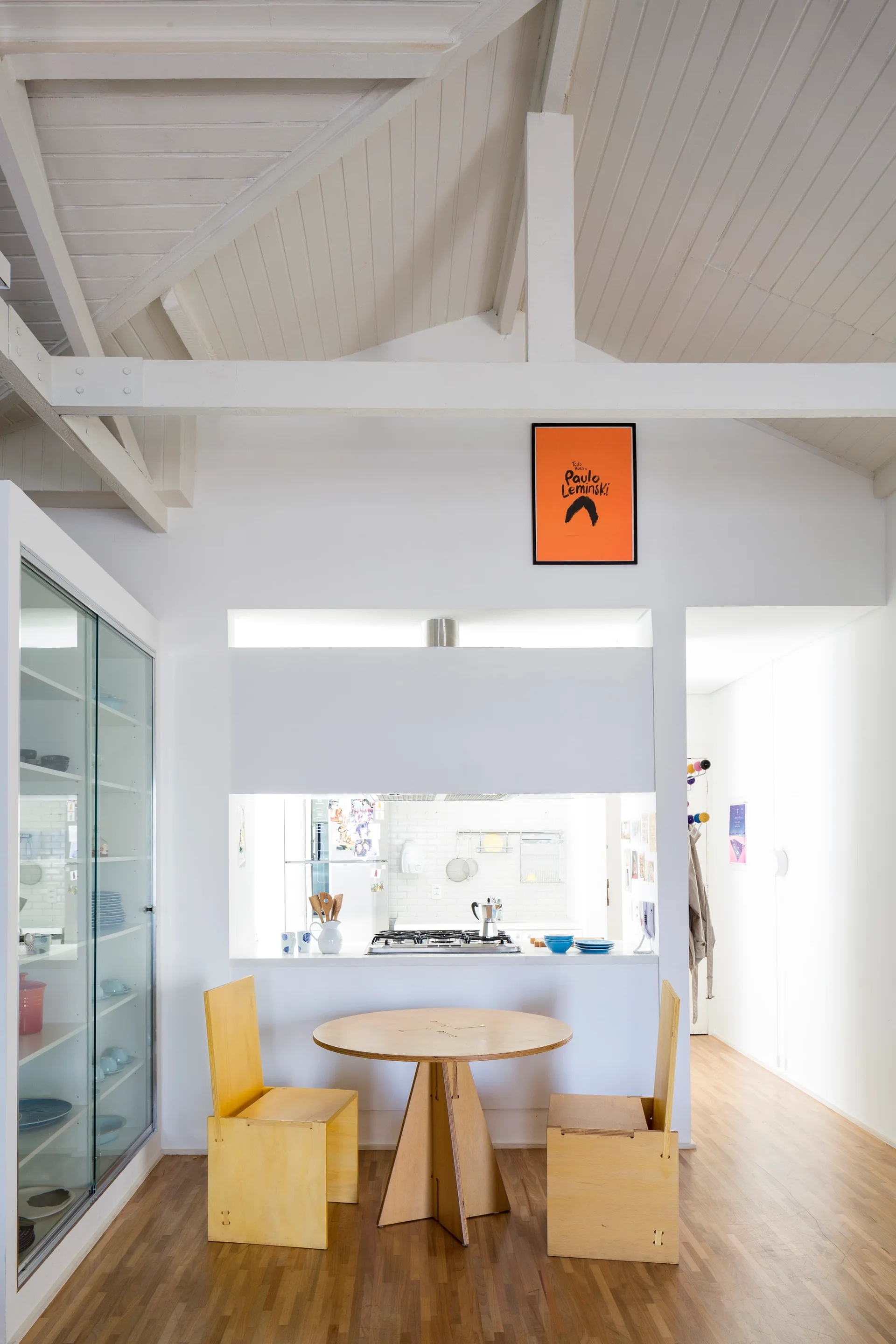 A bright dining area featuring a round wood table with matching chairs next to a pass-through wall showing a kitchen stovetop.