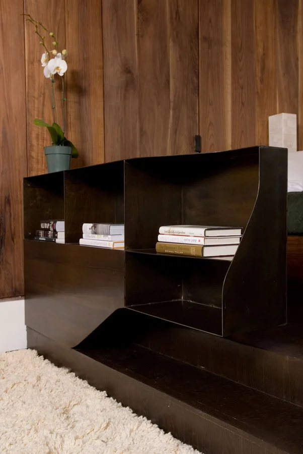 A custom dark metal shelving unit with books sits on a platform next to a vertical wood plank wall and a shag rug.