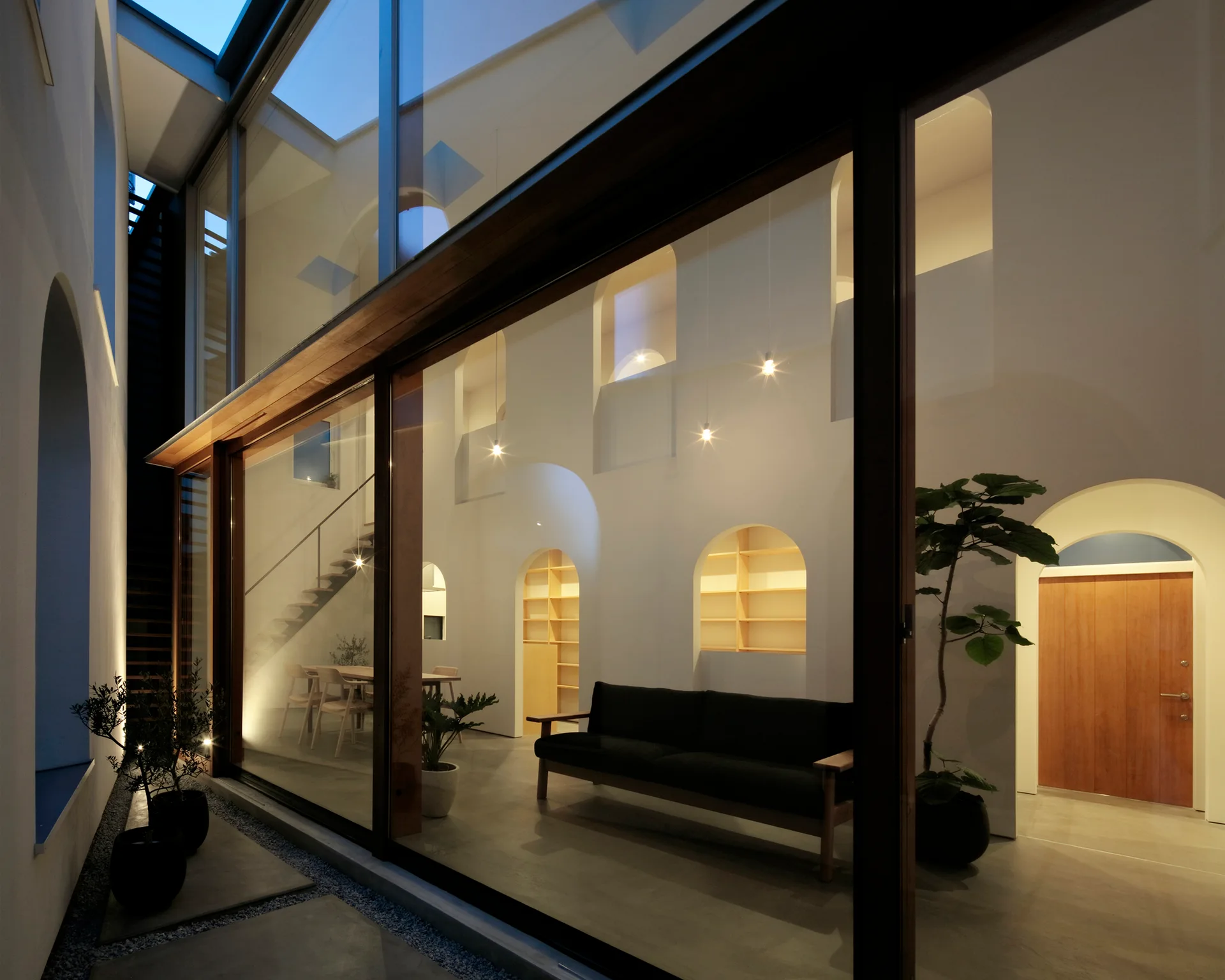 A minimalist living room with arched wall niches and a dark sofa, viewed through a large floor-to-ceiling glass wall.