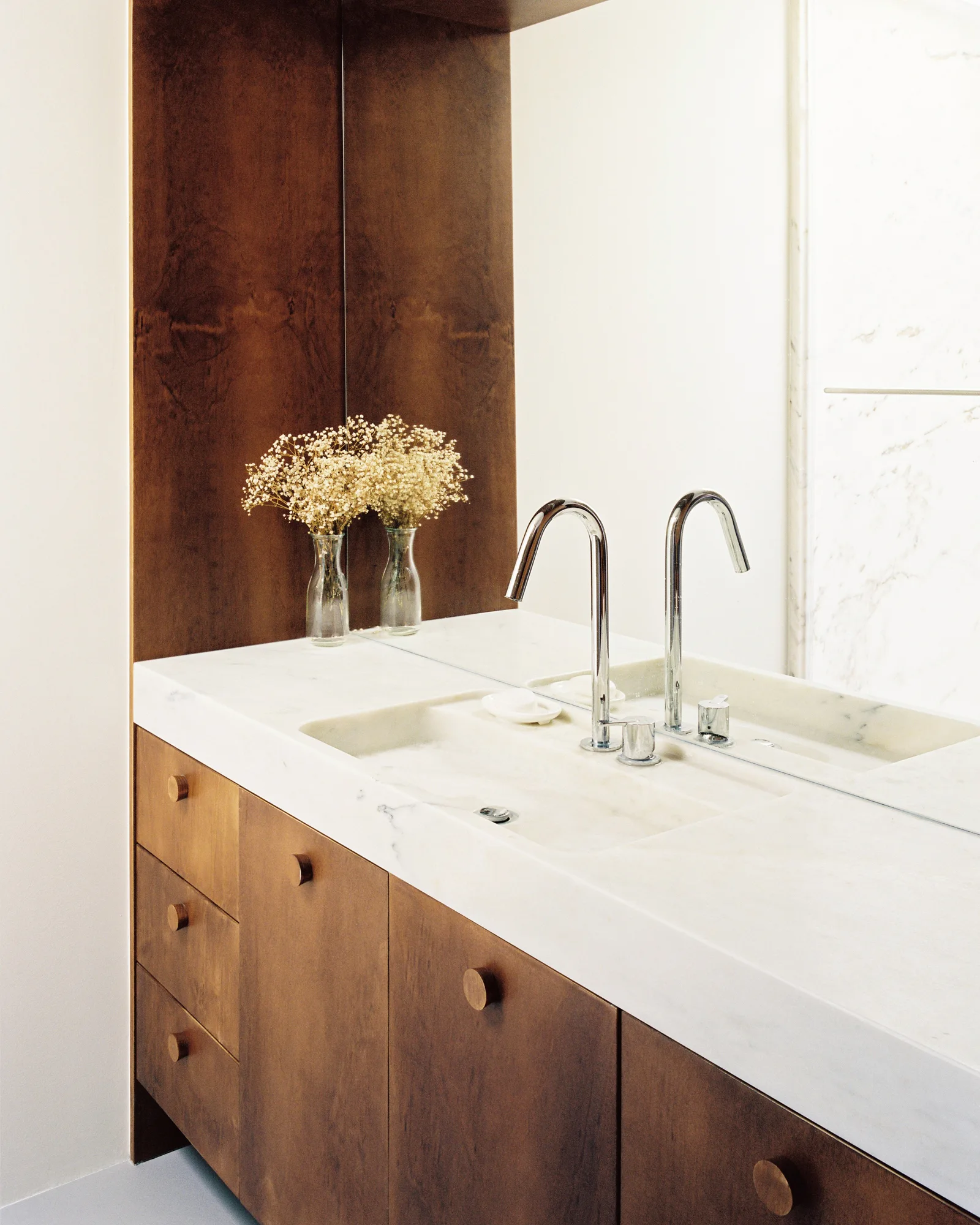 A minimalist wood bathroom vanity featuring a thick white marble countertop with an integrated basin, circular knobs, and a chrome gooseneck faucet.