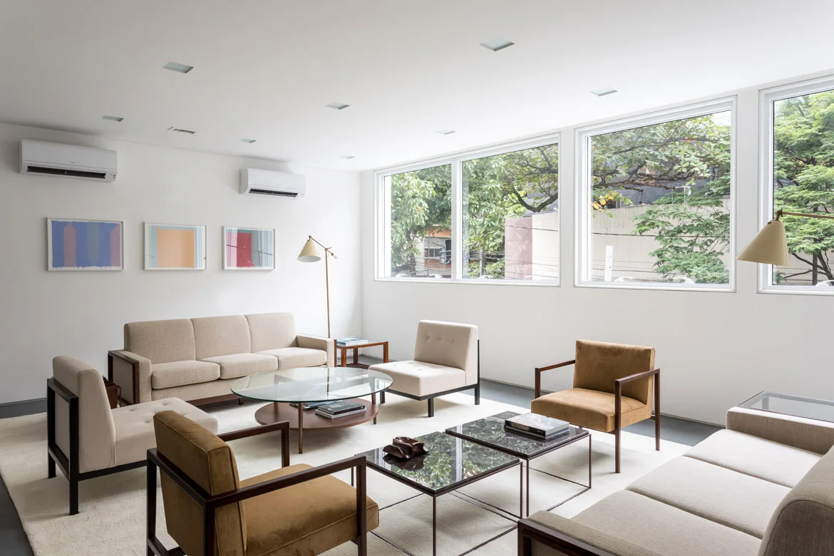 A minimalist living room features beige sofas and ochre armchairs arranged around glass coffee tables on a large white area rug.