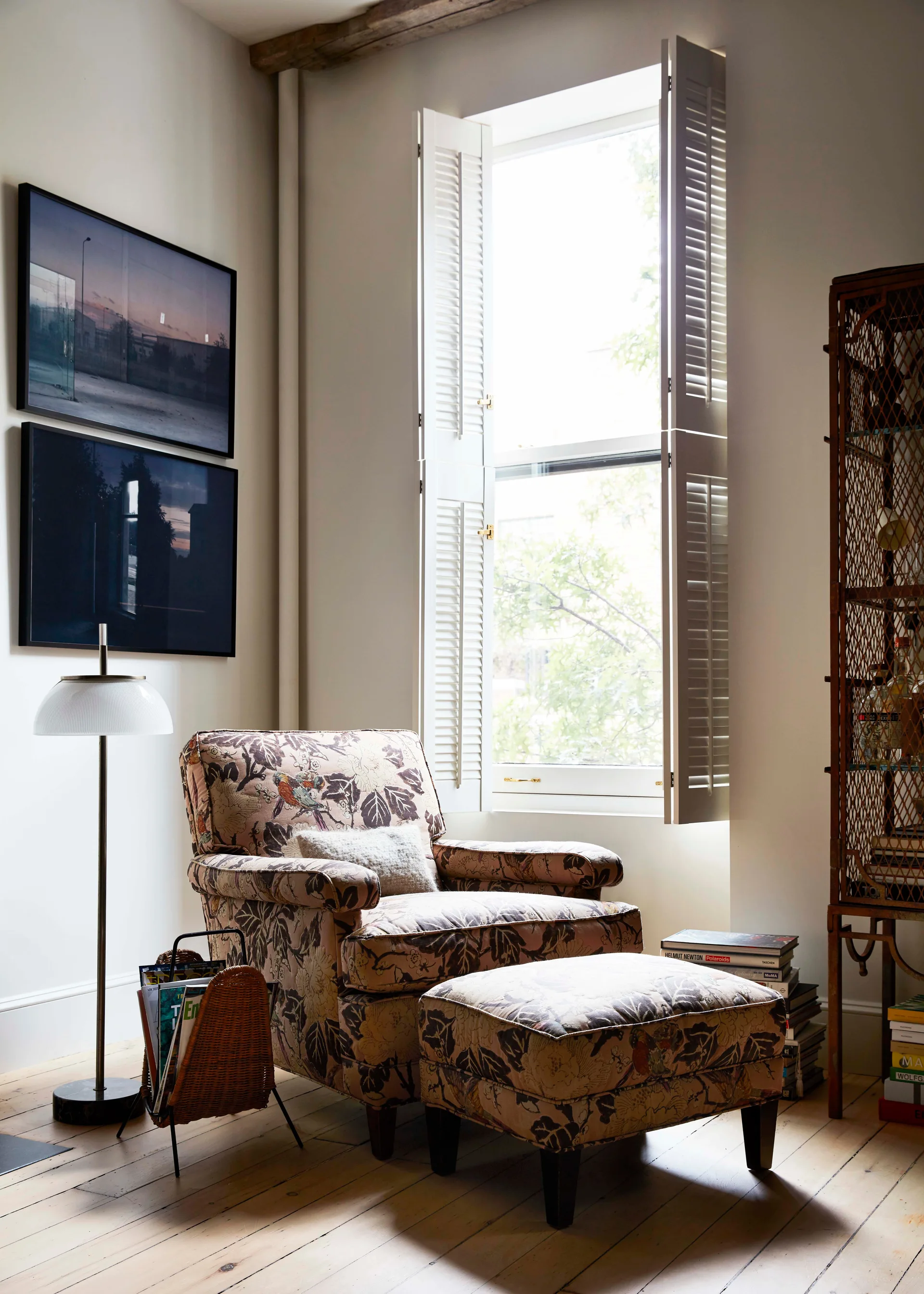 An armchair and matching ottoman with floral upholstery sit on a wood floor next to a window with white shutters.
