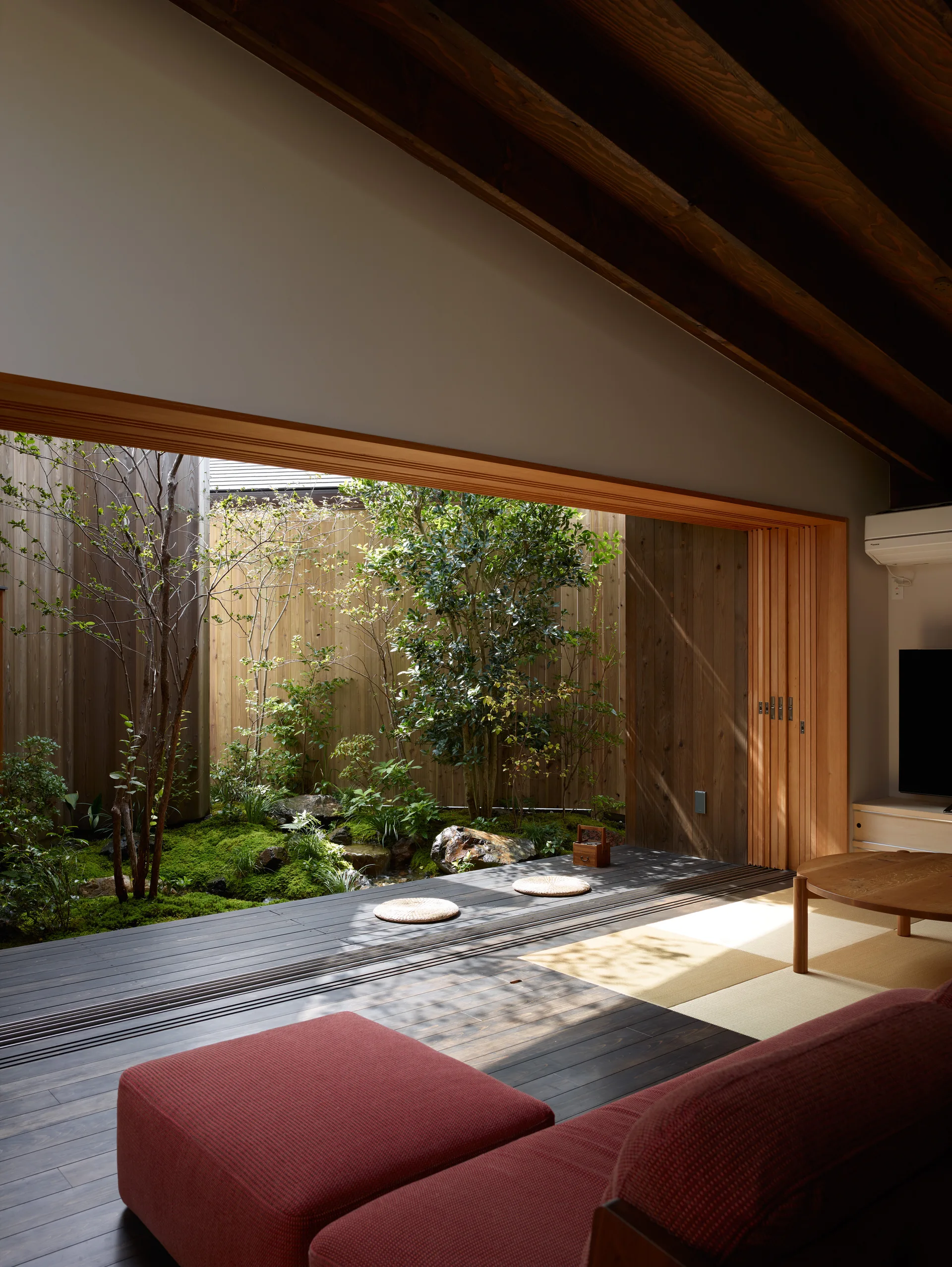A minimalist room with tatami mats, a red sofa, and wide sliding doors opening to an enclosed moss garden courtyard.