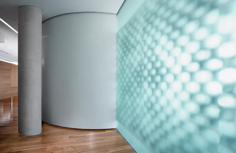A minimalist interior hallway features a cylindrical concrete column, a smooth curved partition wall, and a glowing textured blue glass screen.