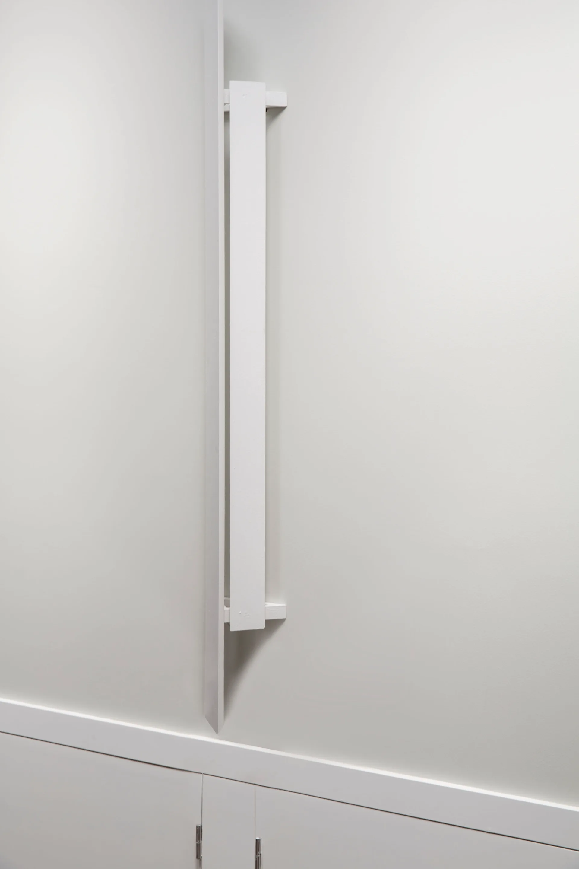A close-up of a white minimalist wooden vertical wall detail mounted above a matching built-in cabinet.