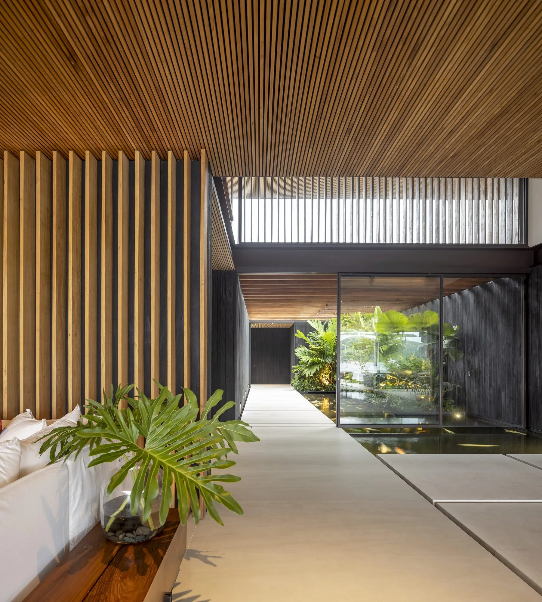 A contemporary hallway featuring a concrete floor, a linear slatted wood ceiling, and an indoor reflecting pool with stepping stones.