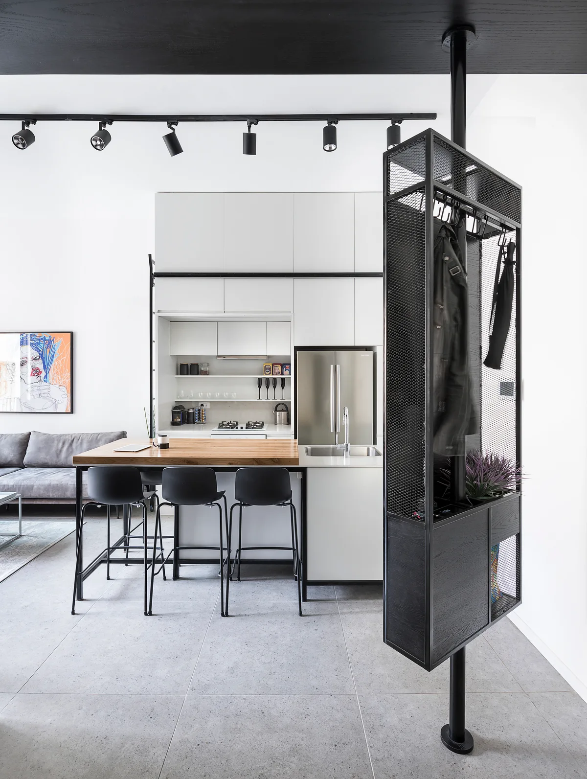 A modern kitchen featuring white flat-front cabinets, a wood-topped island with black stools, and a black metal mesh partition in the foreground.