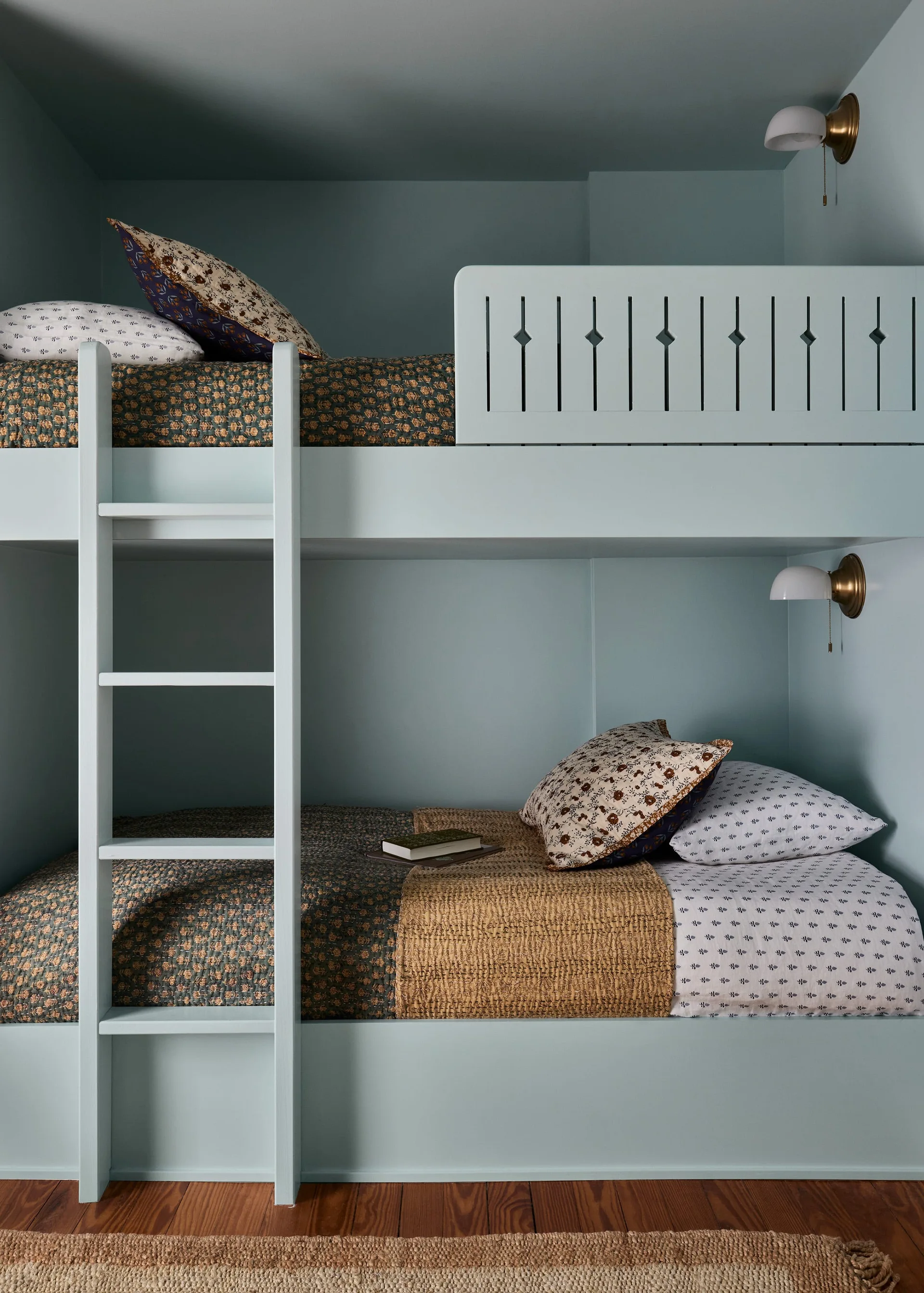 Built-in pale blue bunk beds feature a custom wooden guardrail, an integrated ladder, brass wall sconces, and floral patterned bedding.