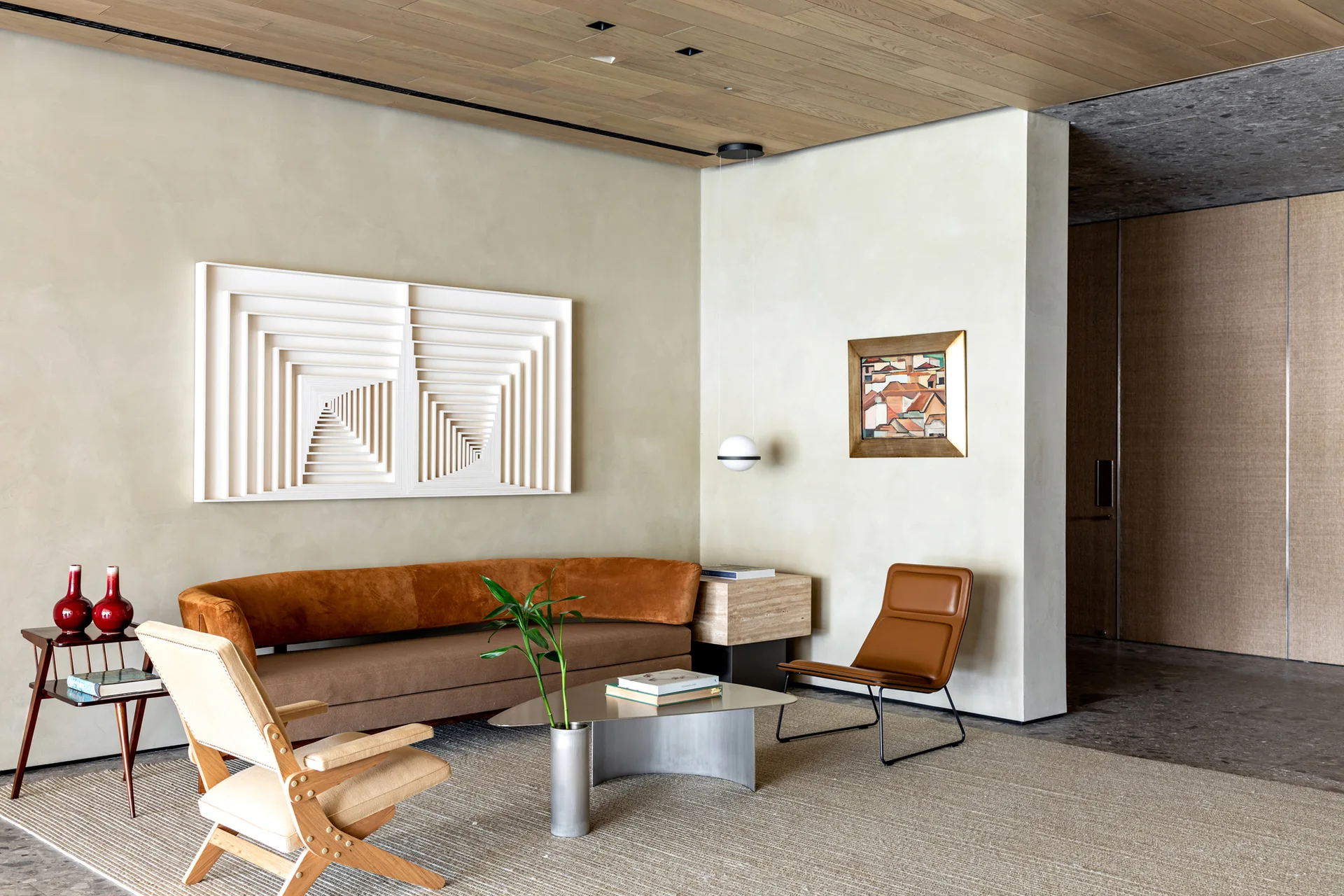 A modern living room features a curved brown sofa, a wood-paneled ceiling, a metal coffee table, and a large white geometric wall sculpture.