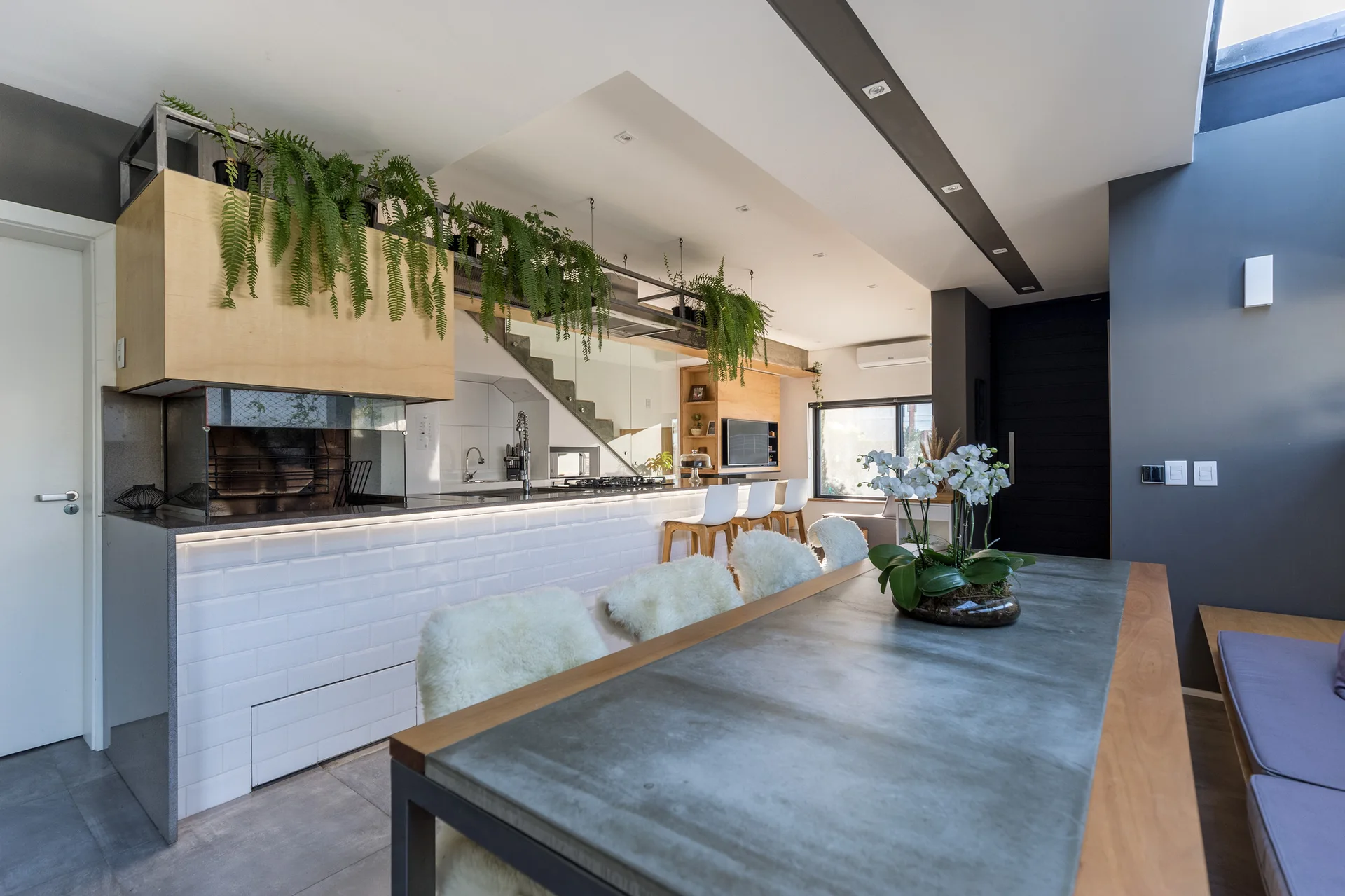 An open-concept kitchen features a white subway-tiled island with hanging ferns above and a dining table with fuzzy-backed chairs.