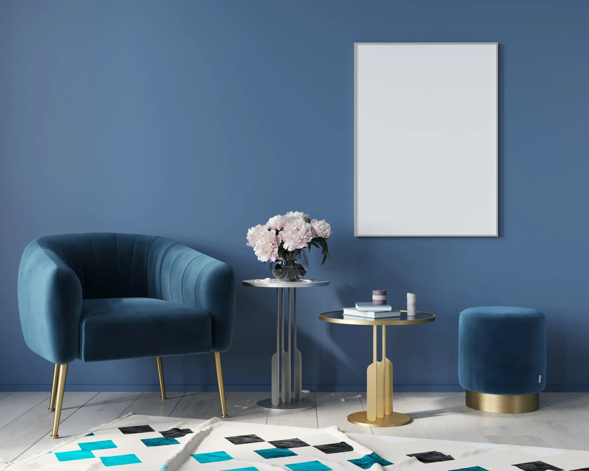 A blue velvet armchair and matching ottoman sit next to gold metal side tables against a solid blue wall holding a large white frame.