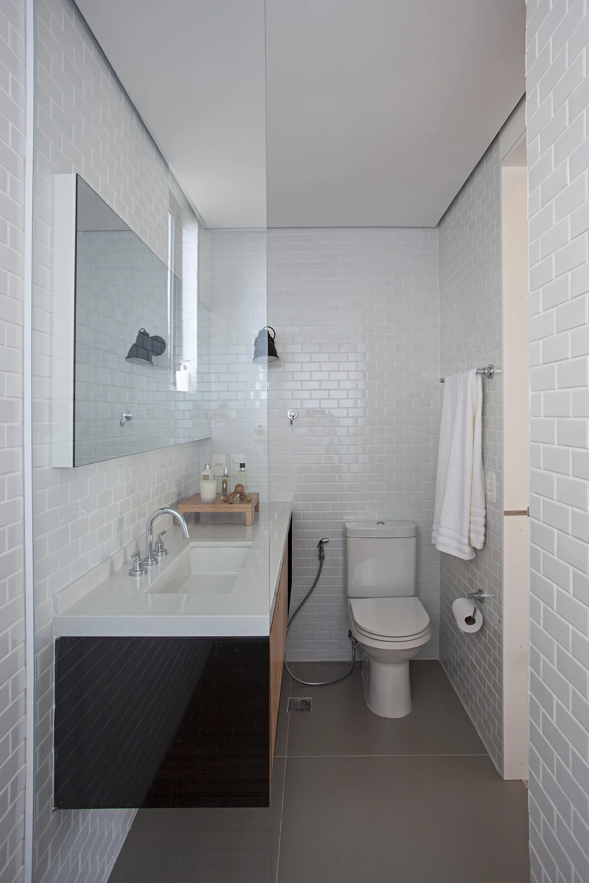 A narrow bathroom features glossy white subway tile walls, a floating dual-tone vanity with a rectangular mirror, and a gray tile floor.