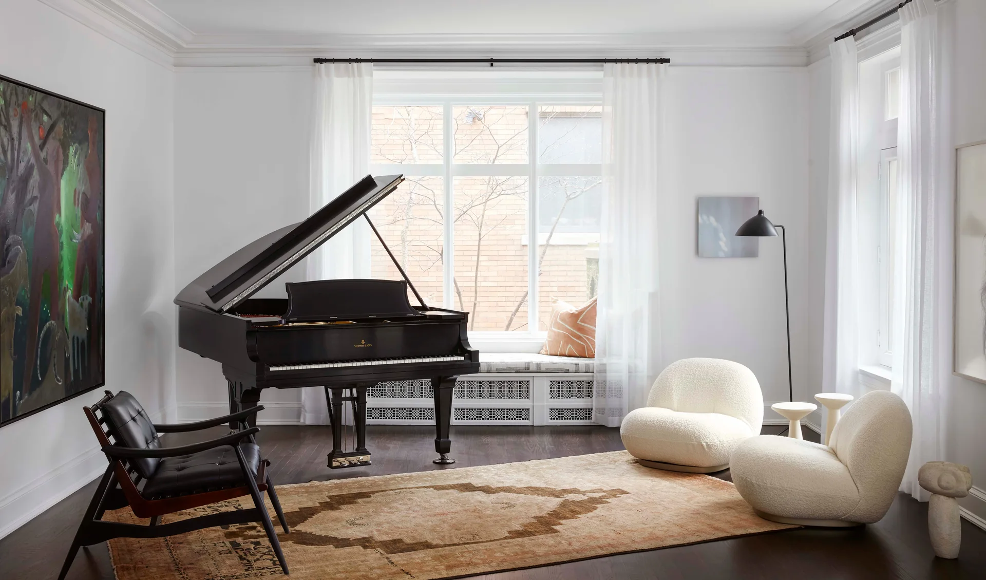 A modern white living room featuring a black grand piano, two curved white bouclé chairs, a leather armchair, and an antique rug.