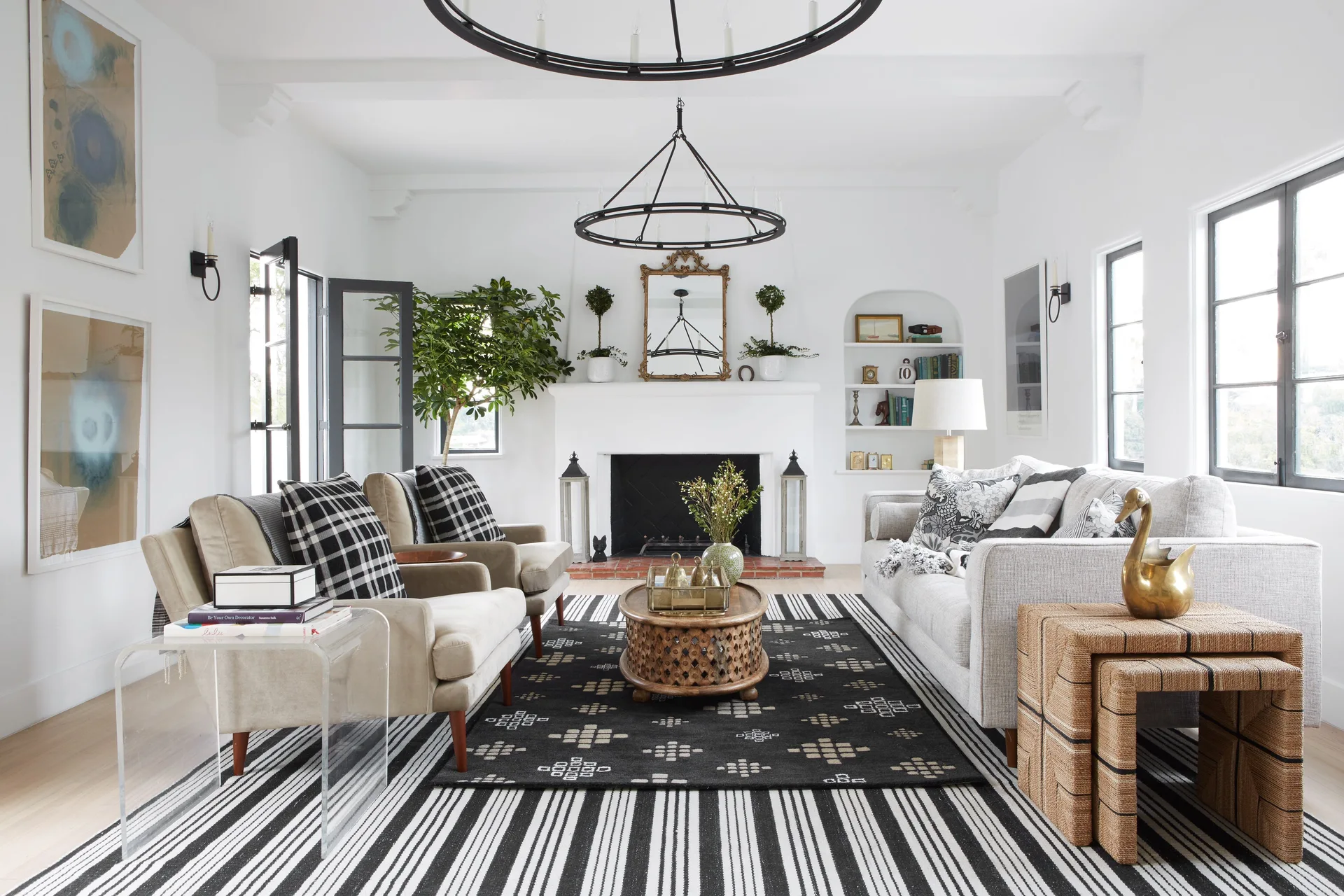 A bright living room features a white fireplace, arched built-in shelving, two armchairs, a sofa, and a large black and white striped rug.