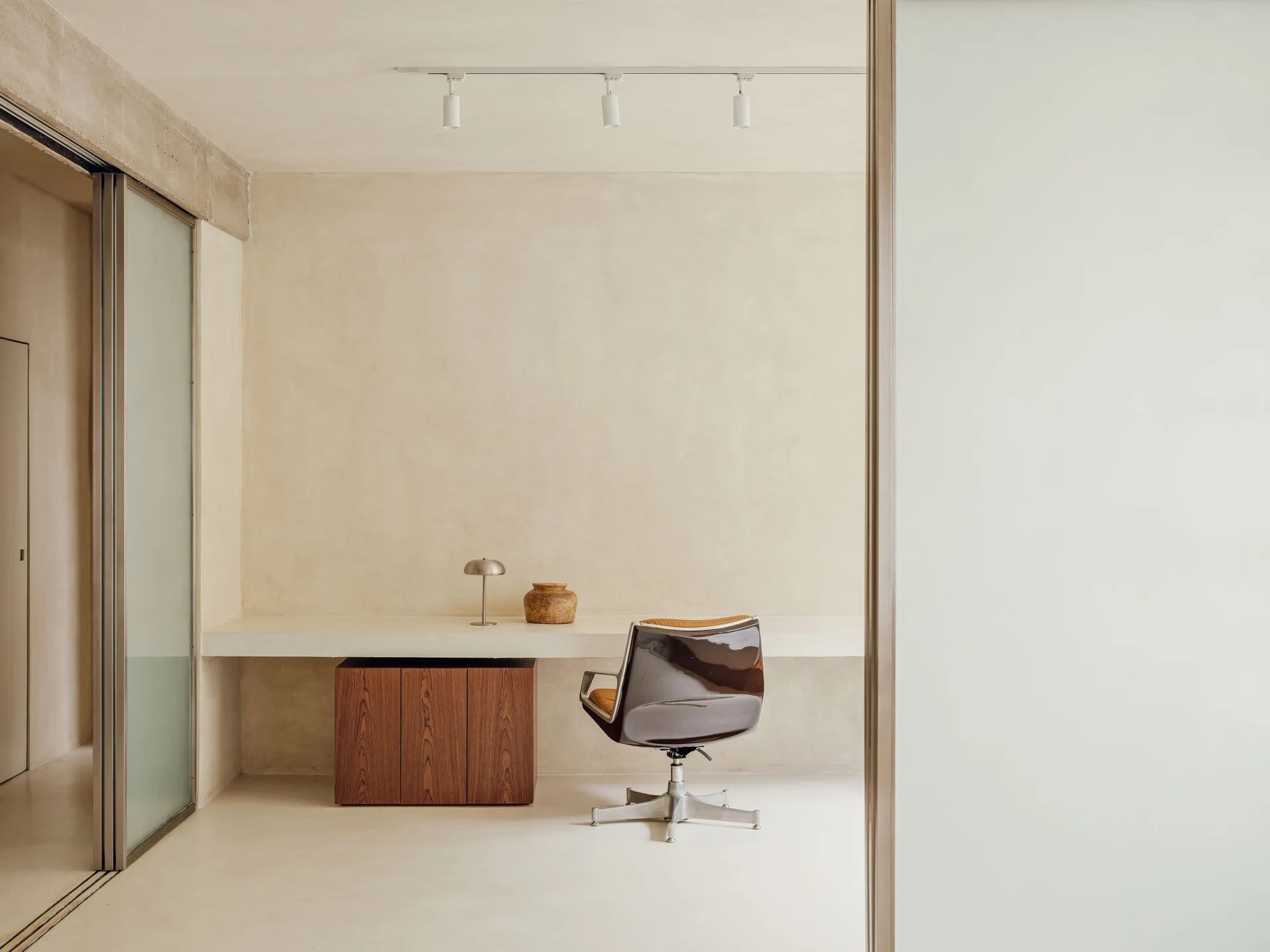 A minimalist home office featuring a floating white desk with a wood cabinet underneath, set against beige textured plaster walls.
