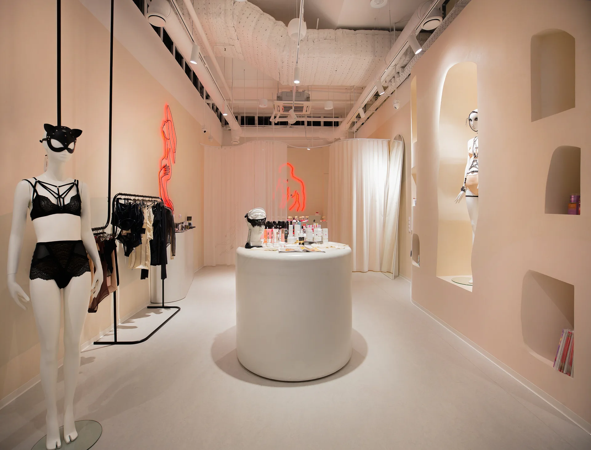 A minimalist pink-toned boutique interior features arched wall niches, mannequins, a white circular display counter, and glowing neon silhouette art.