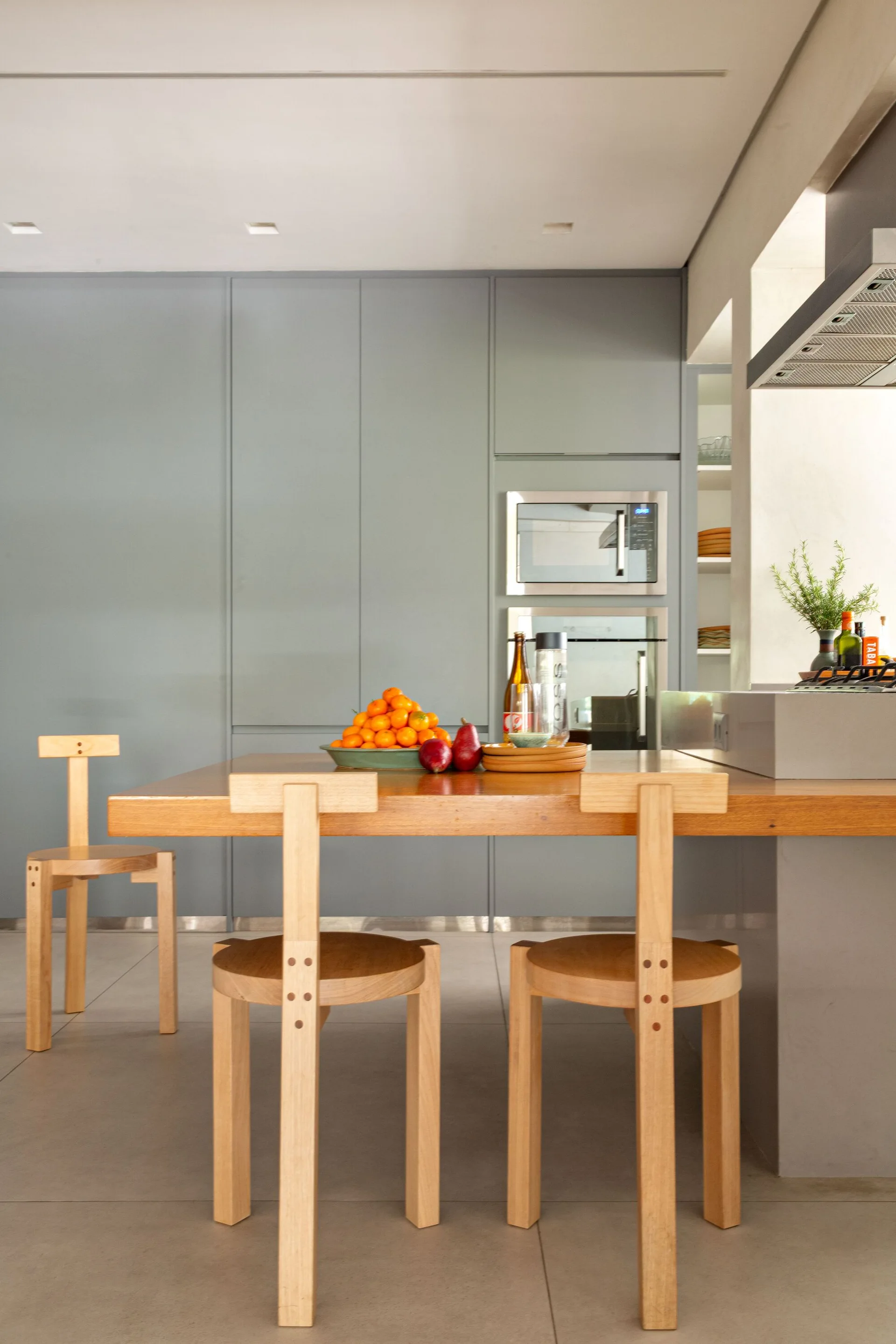 A minimalist grey kitchen features flat-front cabinets, built-in appliances, and an integrated wood dining table with matching wooden stools.
