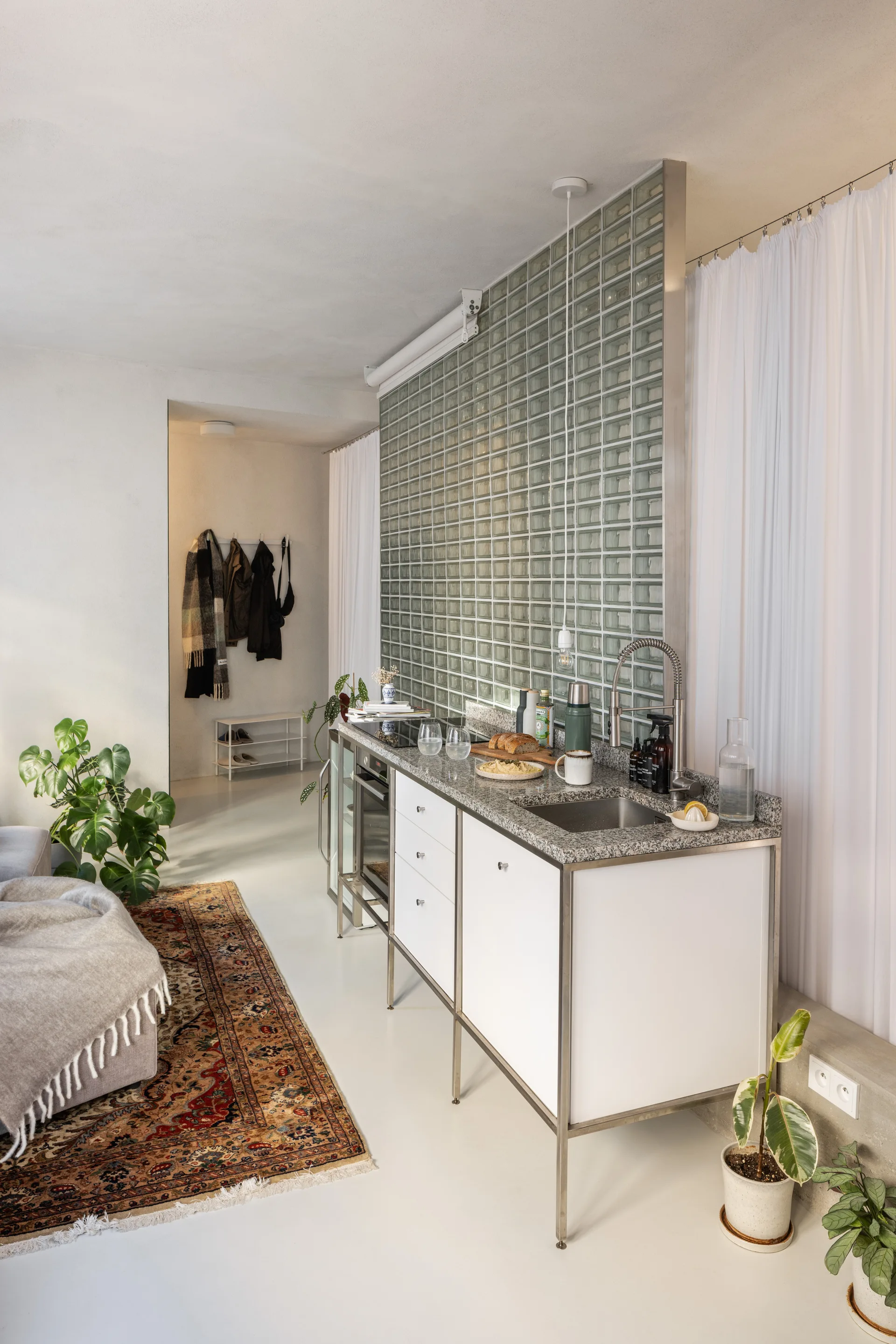 A metal-framed kitchen island with white cabinets sits in front of a glass block partition wall beside a patterned rug.
