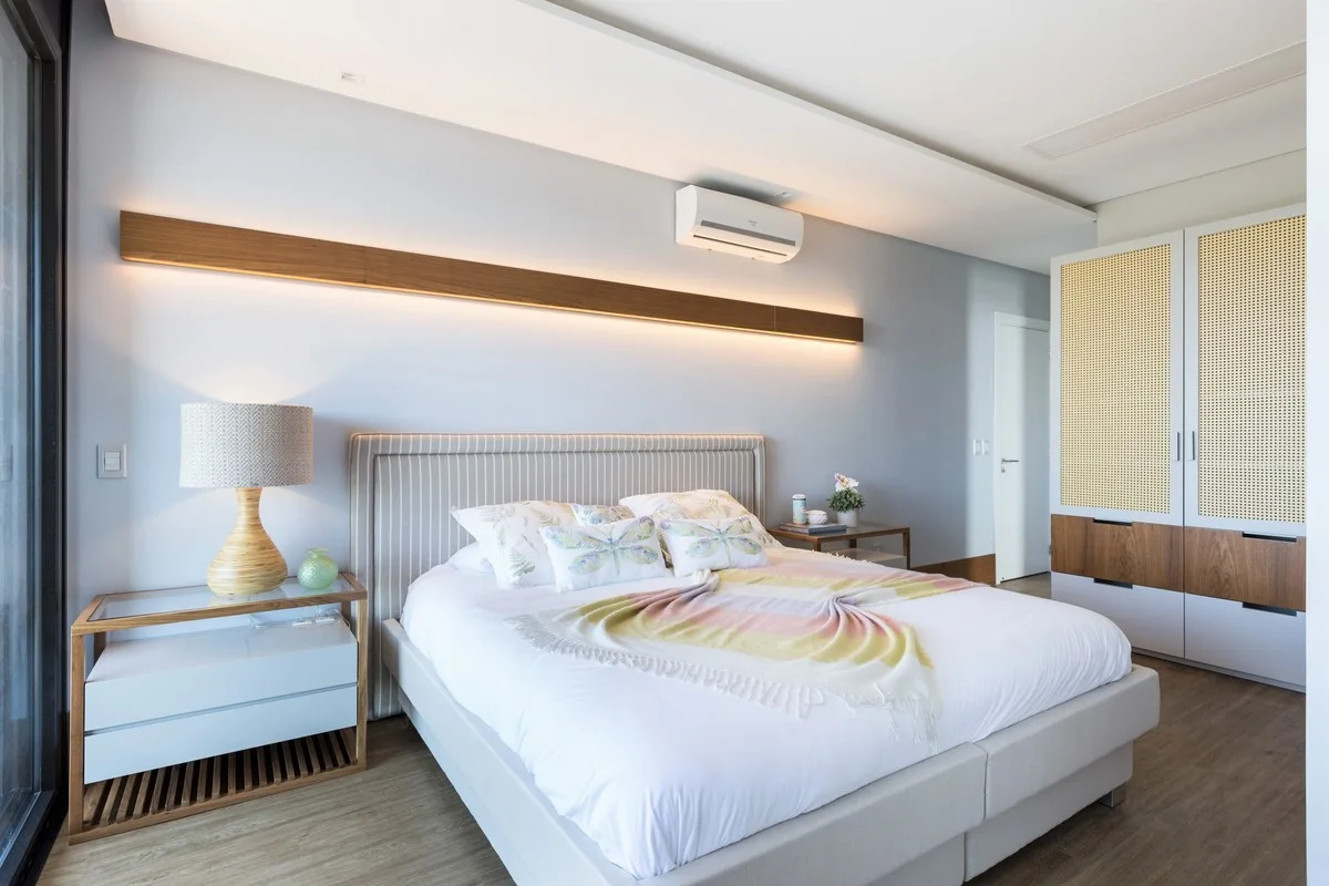 A modern bedroom featuring a bed with a striped headboard, a floating wood light bar, and a white built-in wardrobe with cane door panels.
