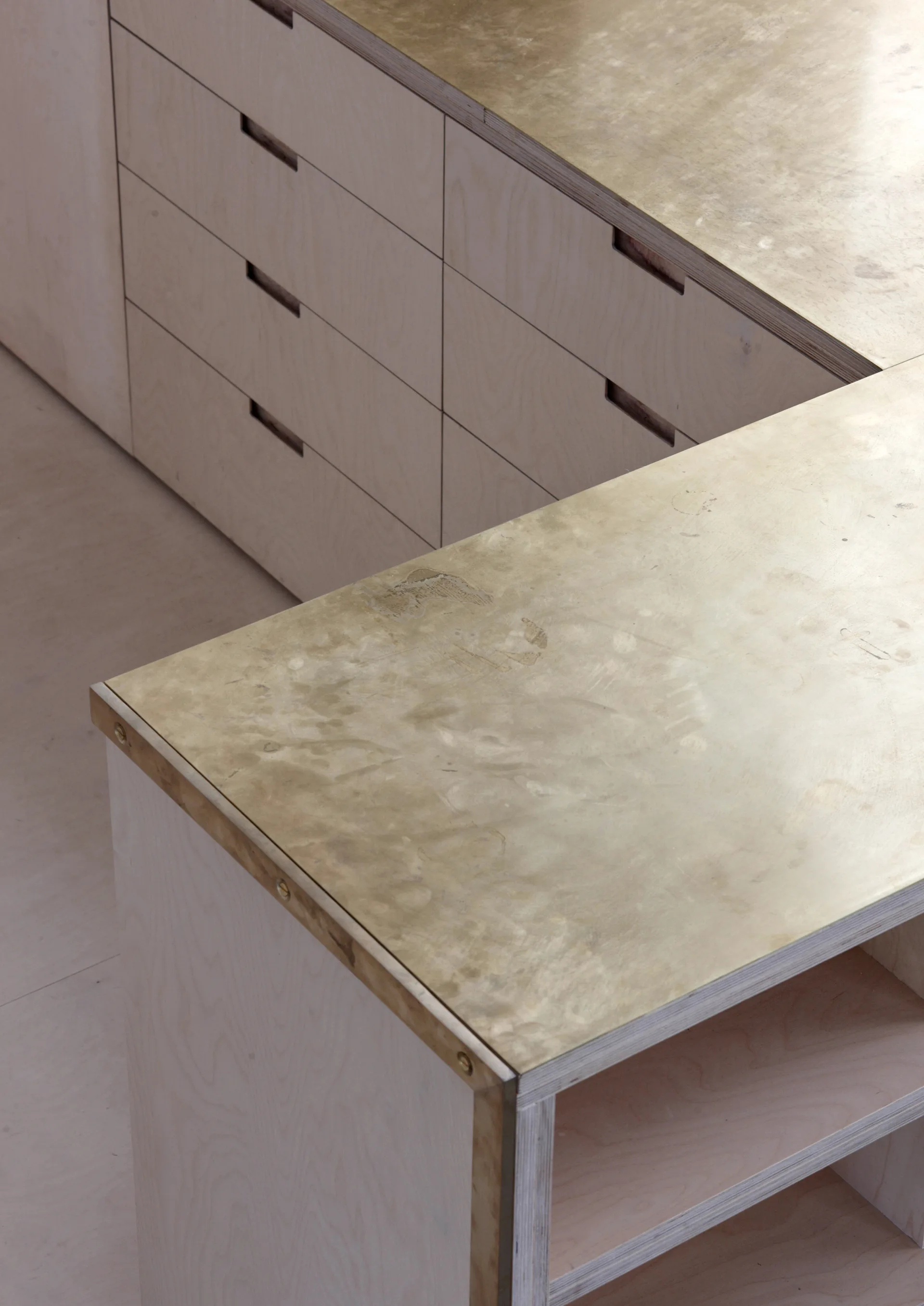 A close-up shot of custom light plywood drawers with recessed cut-out handles and a patinated brass-plated countertop.