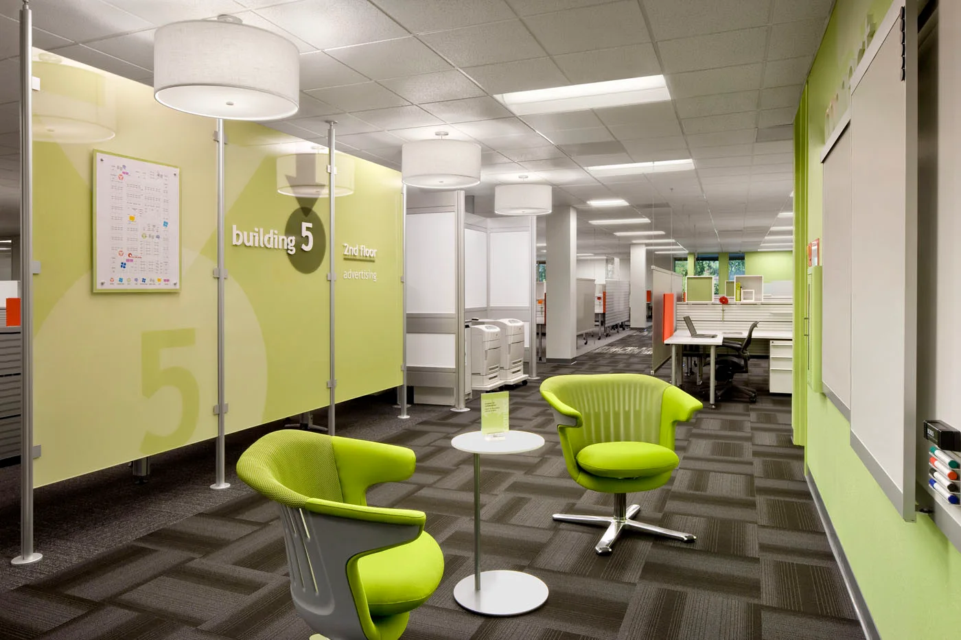 A commercial office waiting area features lime green armchairs, green glass partitions, and large white drum pendant lights on a gray carpet.